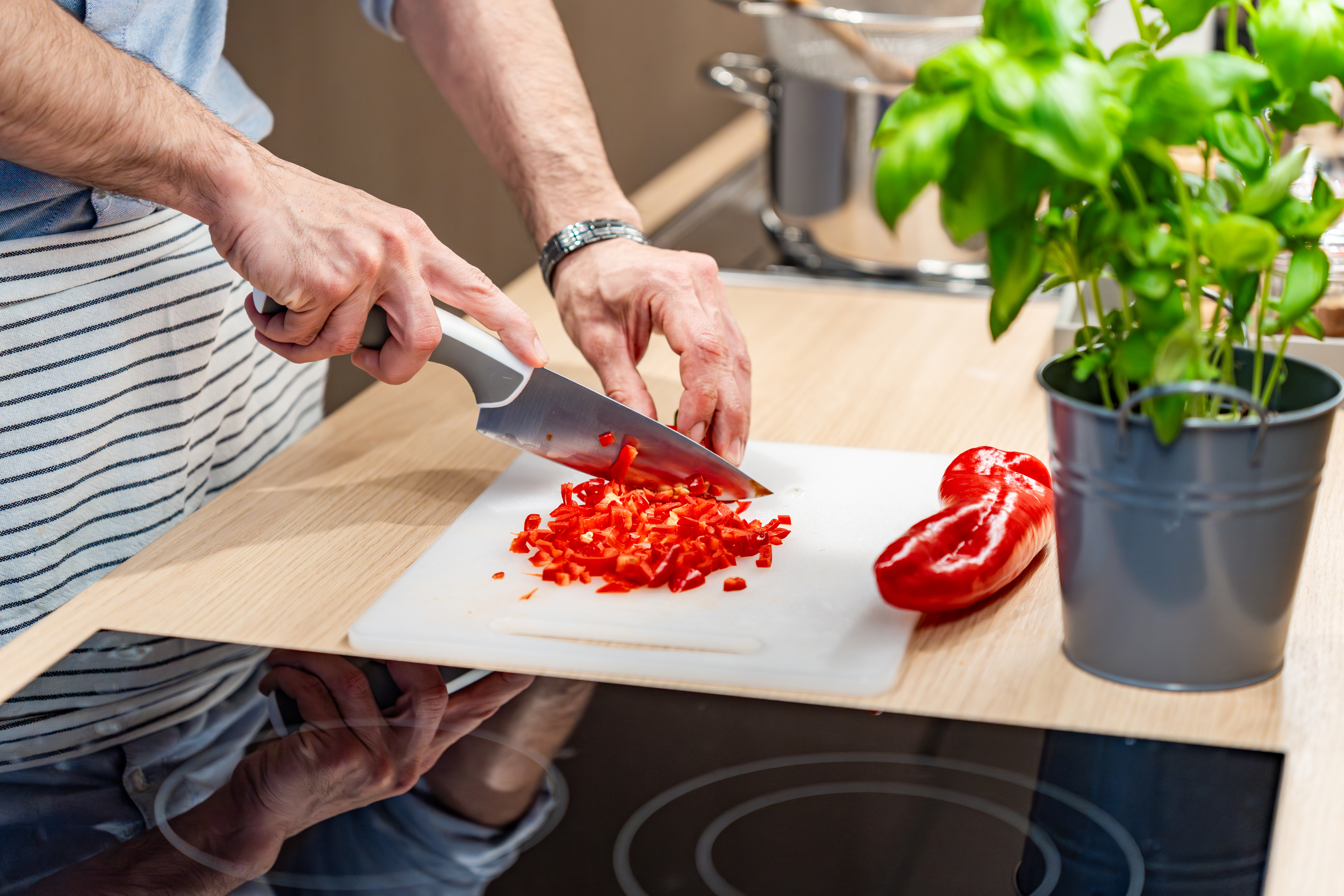 Ansicht von zwei Händen eines R4R Bewohners, der eine rote Paprika auf einem weißen Schneidbrett in der Küche schneidet.