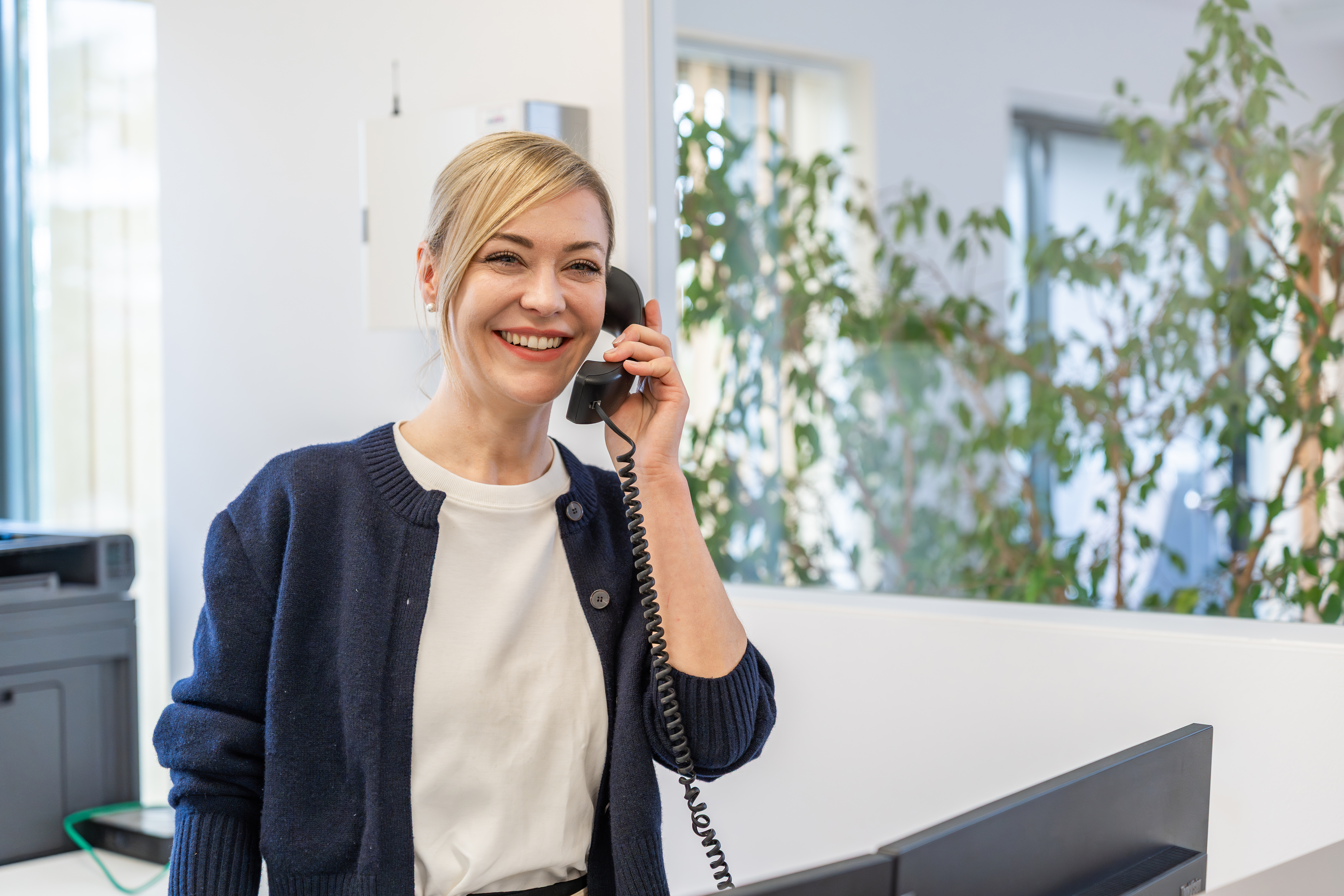 Eine lächelnde R4R Office Managerin telefoniert stehend in ihrem Büro.