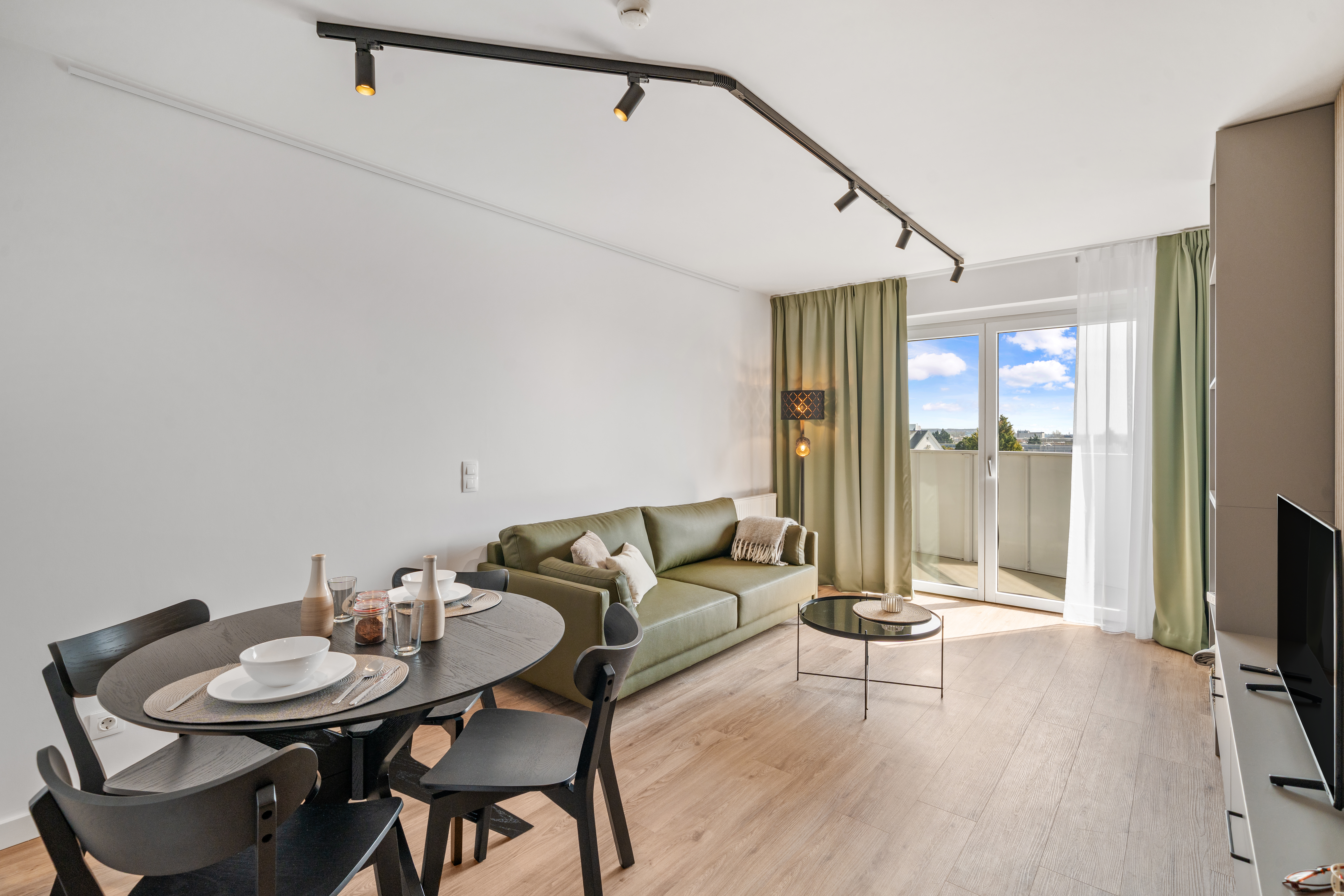 Modernes Apartment mit grünem Sofa, Essbereich mit rundem Tisch und Terrassenzugang