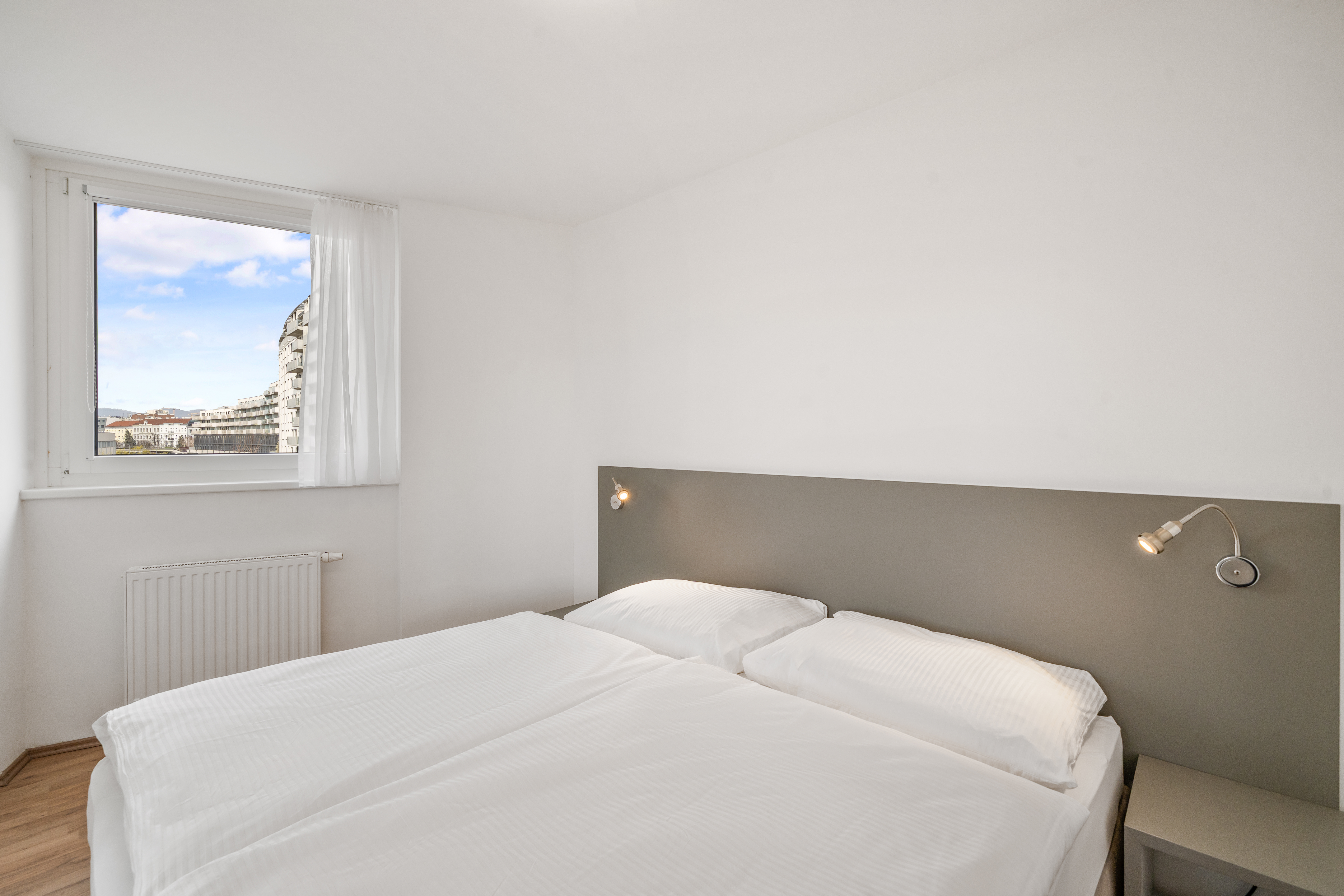 Schlafzimmer mit Doppelbett und Fensterblick auf Wien in einem Room4Rent Serviced Apartment Typ L