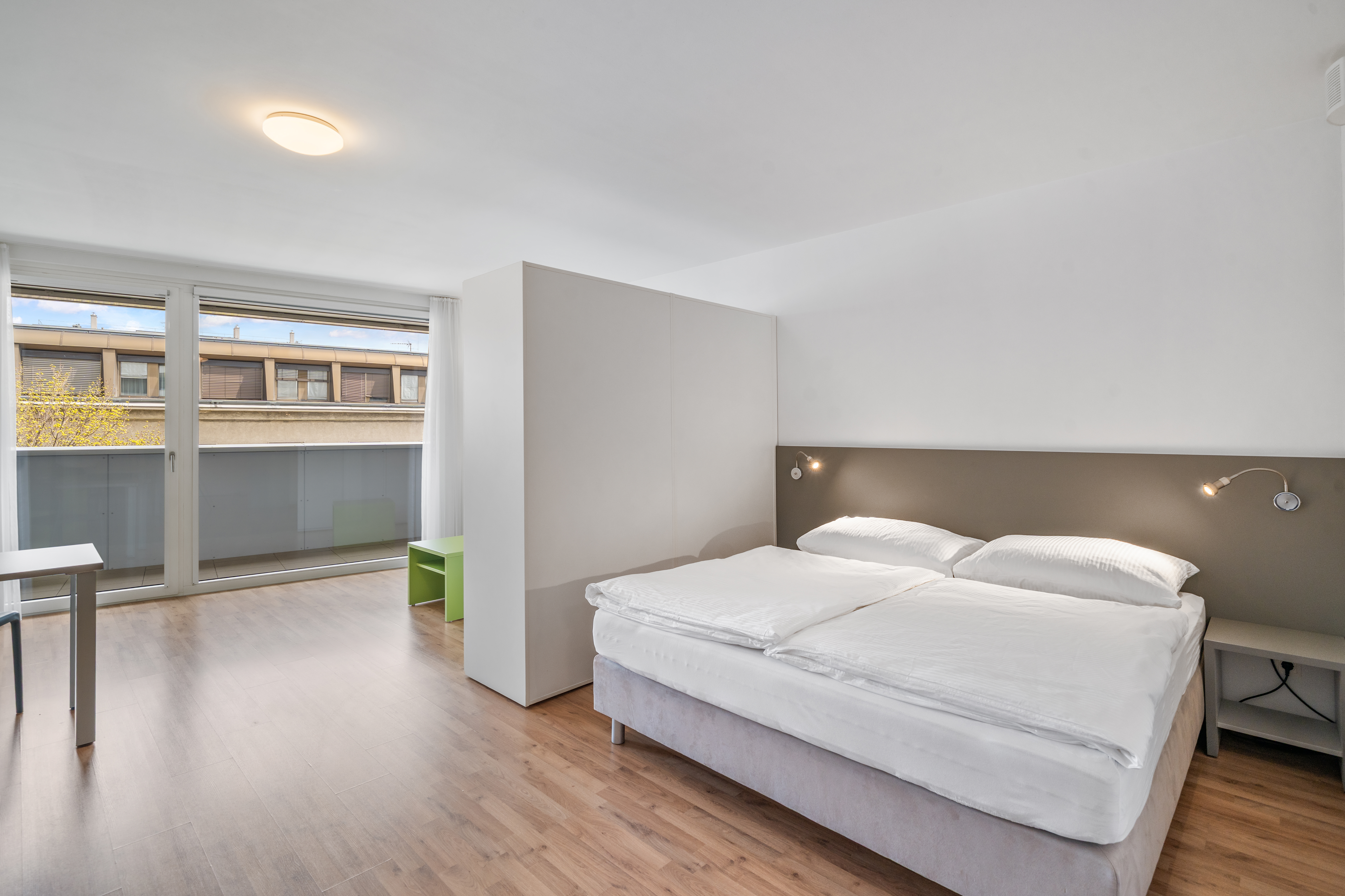 Schlafzimmer mit Doppelbett, Nachtschränke, große Fenster mit Außenblick, helle Decke mit Leuchte