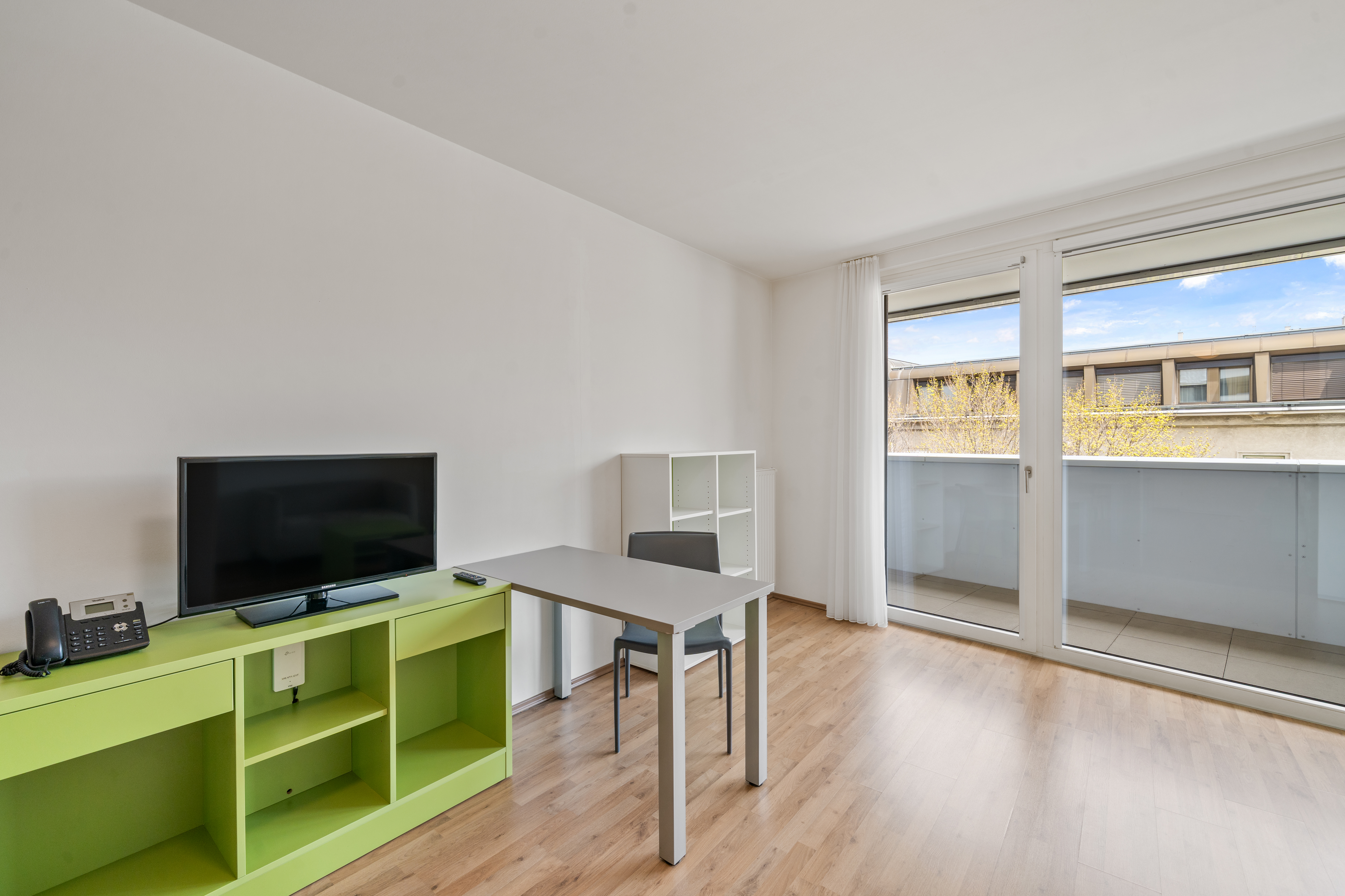 Leerer Apartmentbereich mit grünem TV-Möbel, Schreibtisch und modernem Mobiliar
