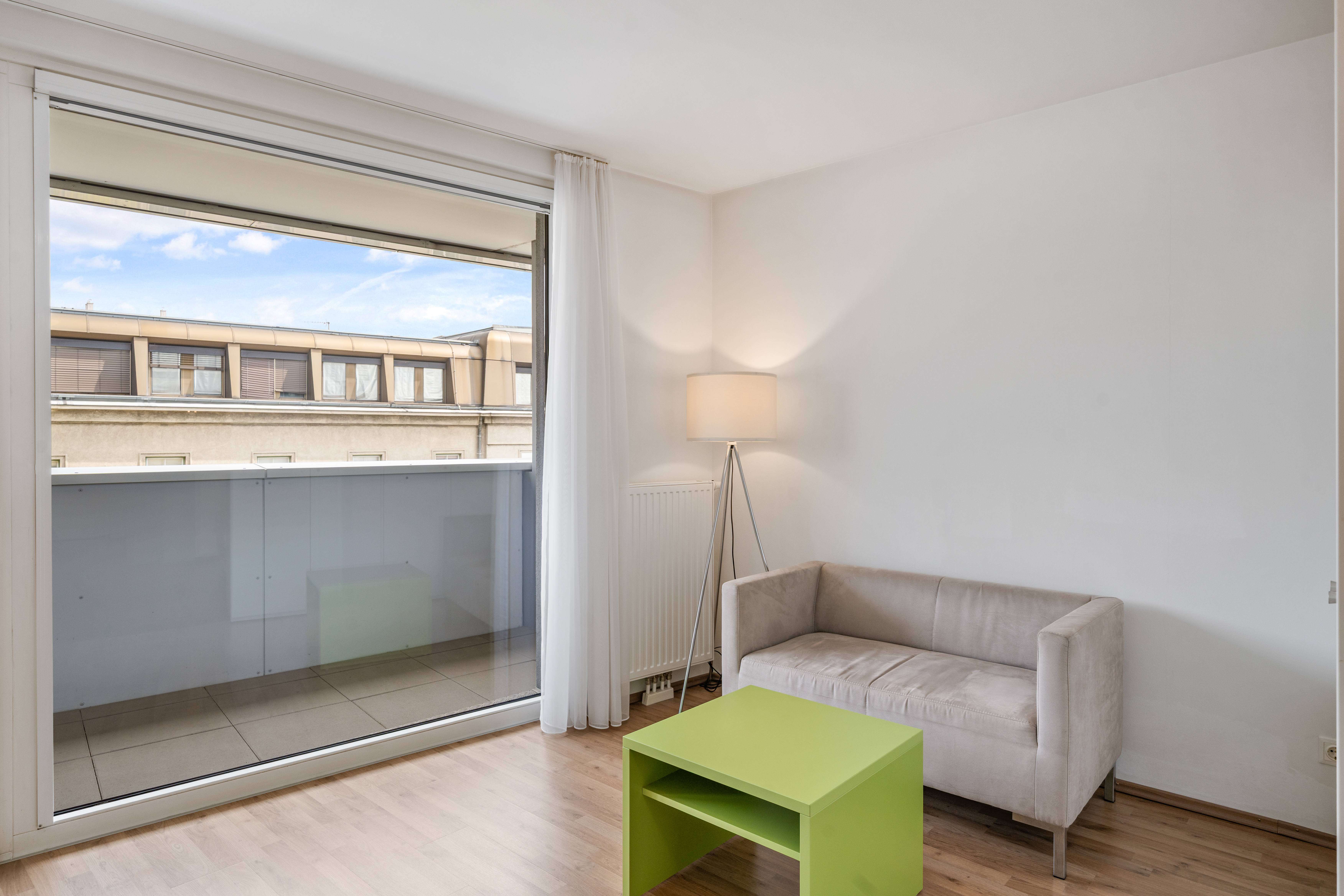 Wohnbereich mit beigem Sofa, grünem Couchtisch und großem Fenster zur Terrasse