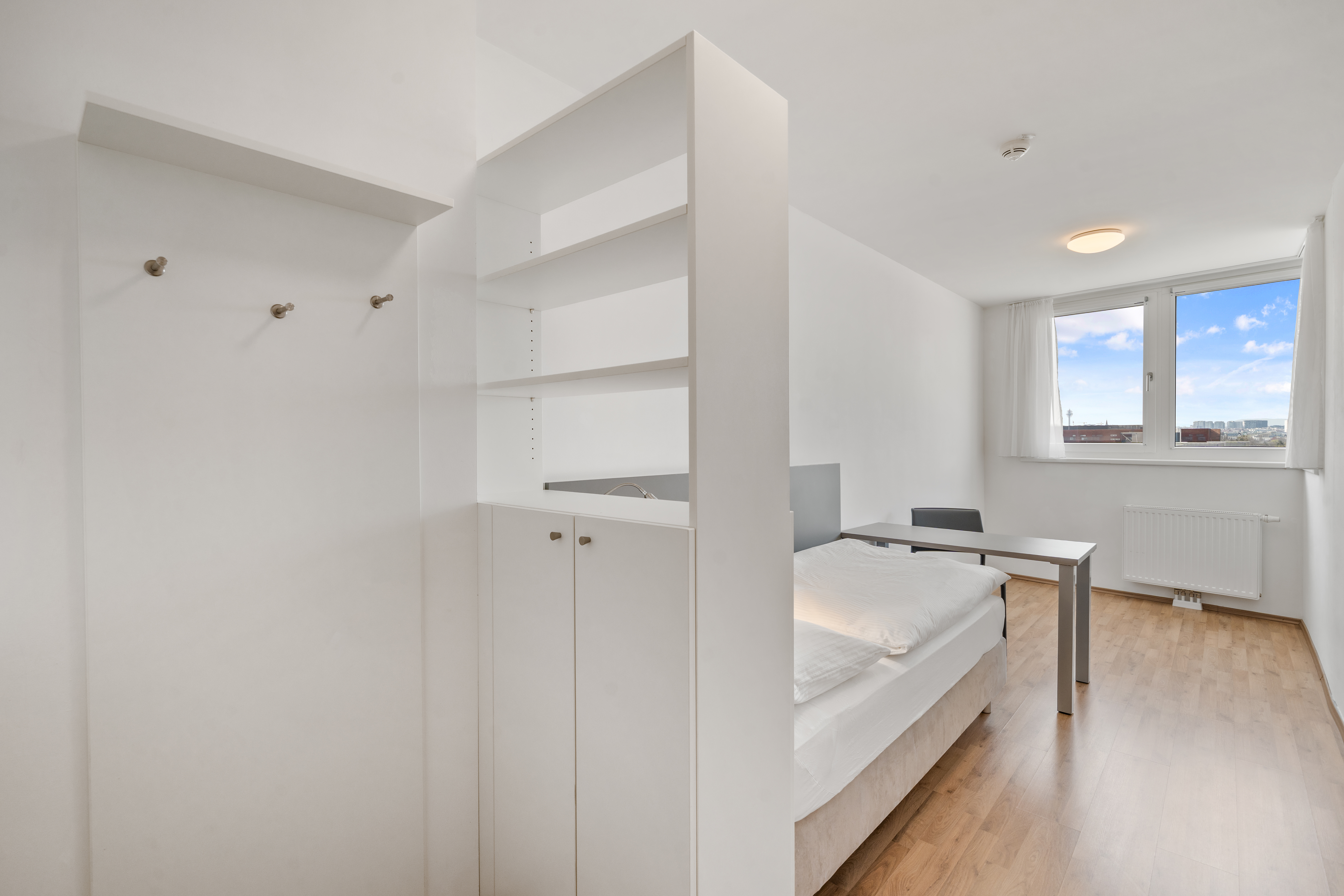 Leeres Apartment Typ XL mit offenem Wohnbereich, Schlafnische, Arbeitstisch und großer Fensterfront mit Stadtblick