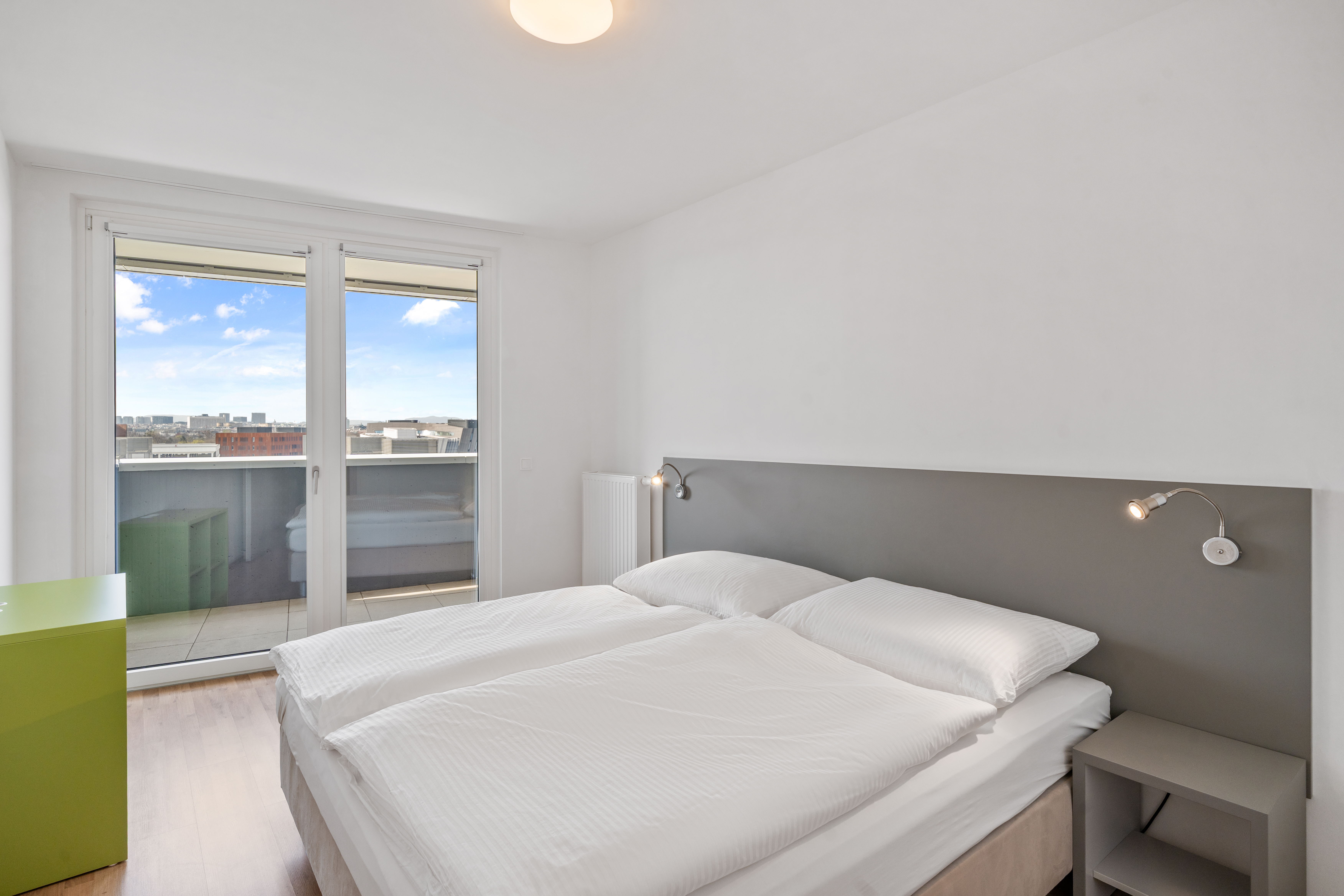 Schlafzimmer eines XL Apartments mit Doppelbett, großem Fenster und Stadtblick