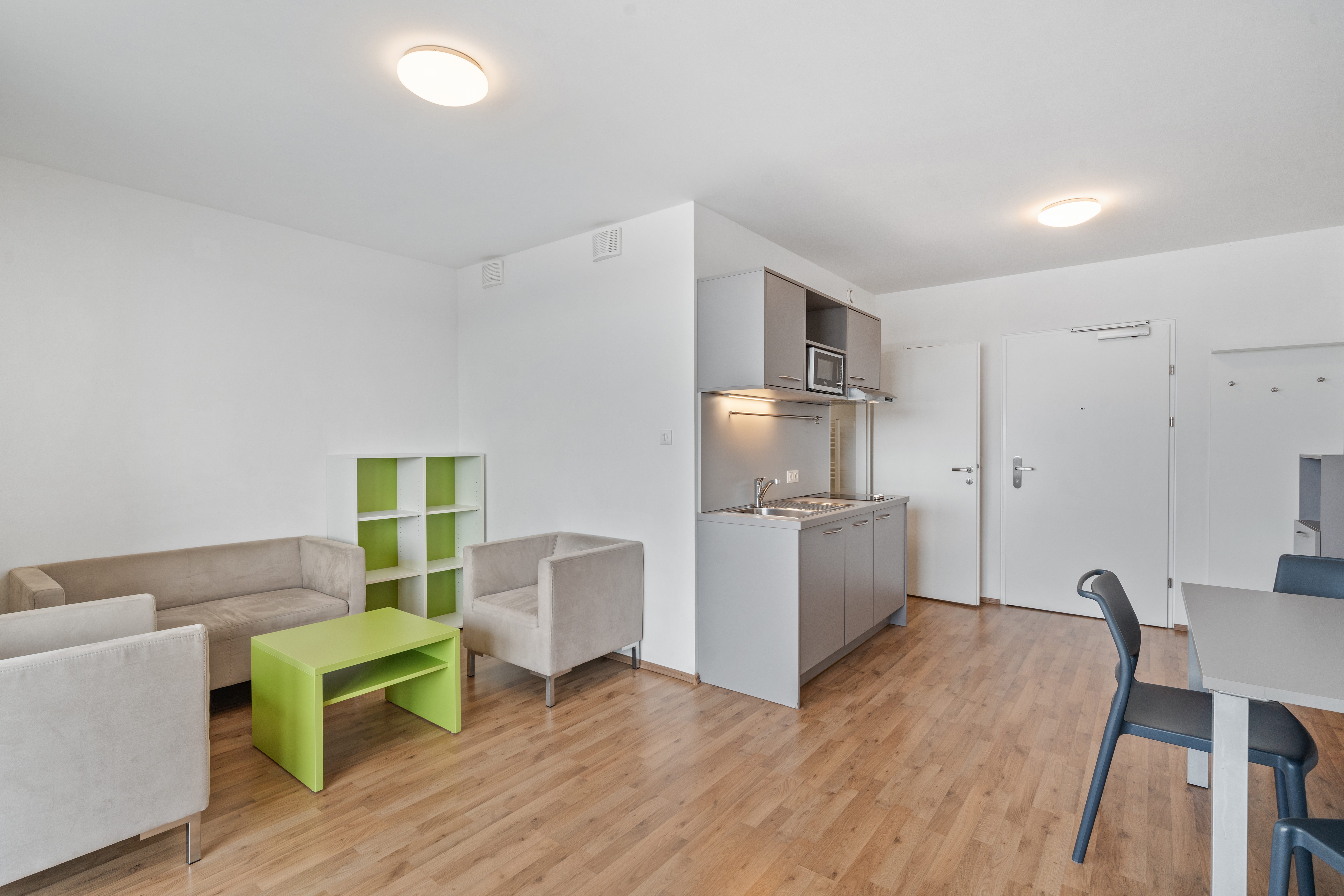 Wohnbereich mit beigen Sofas, grünem Couchtisch und offener Küchenzeile in einem möblierten XL Apartment