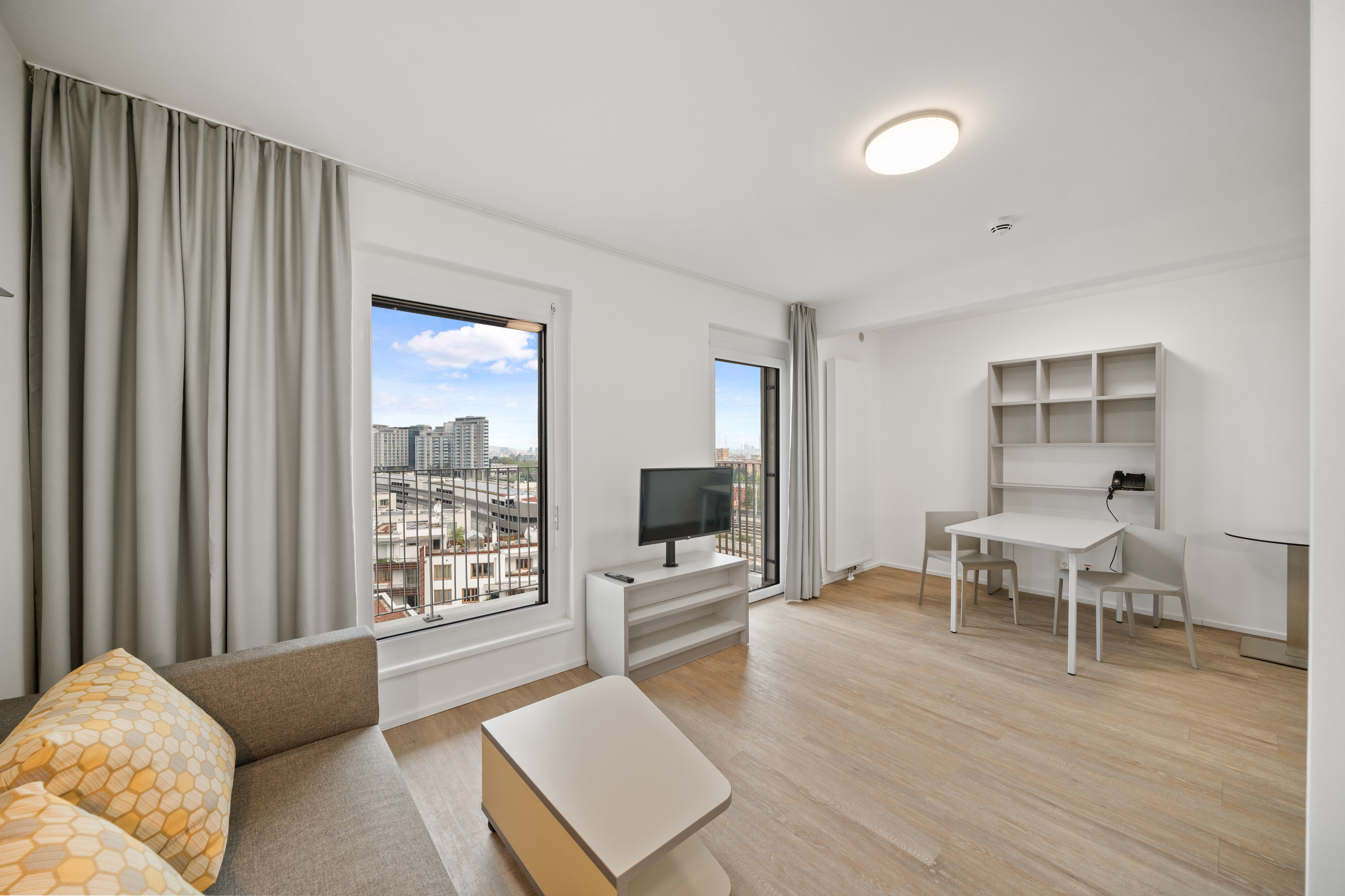 Wohnbereich eines Room4Rent Typ L Apartments in der MusicBox Wien mit großem Panoramafenster, Sessel und Esstisch
