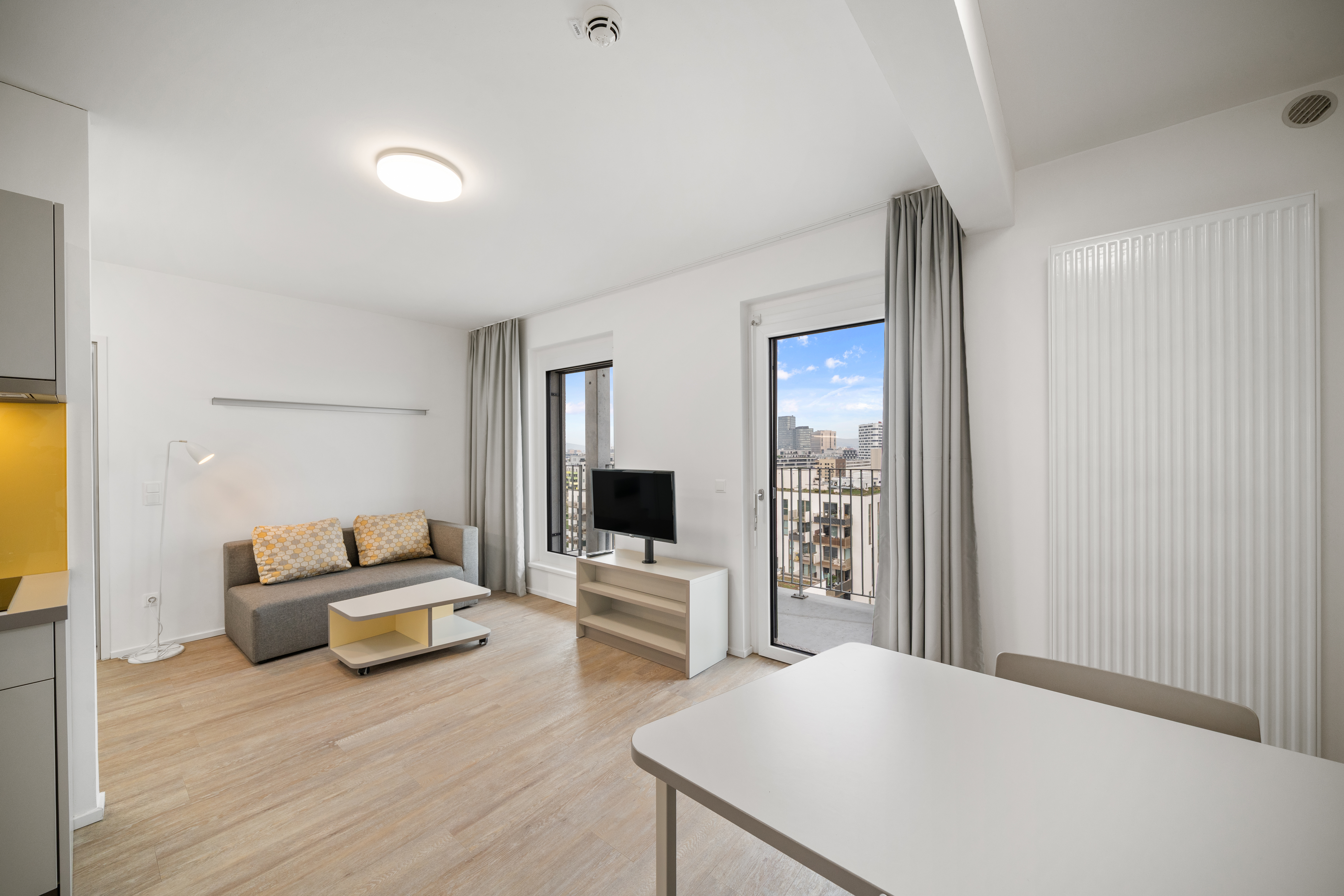Offener Wohn- und Essbereich mit Küche, Sofa und Balkonzugang im Room4Rent Typ L Apartment in der MusicBox Wien