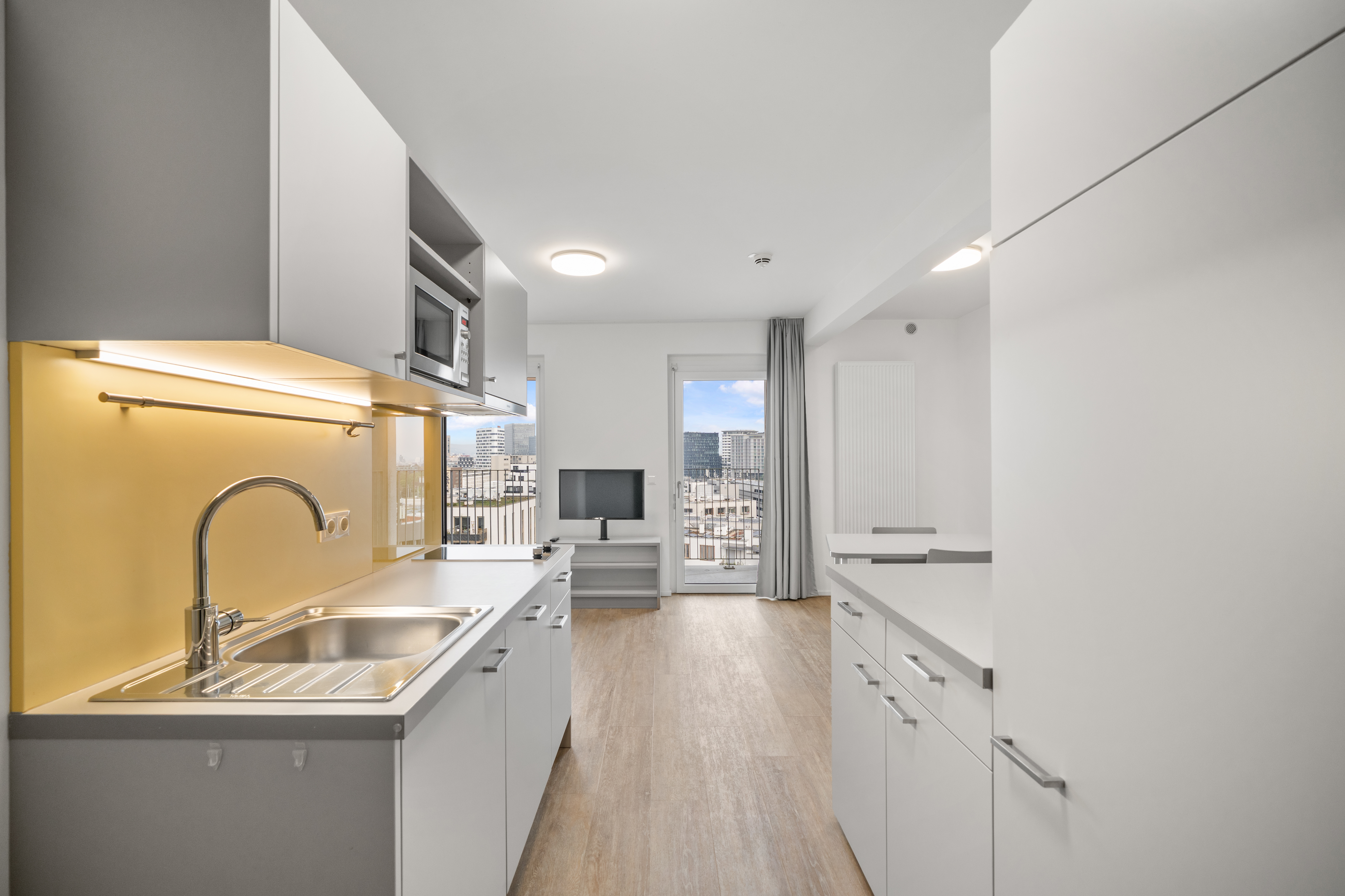 Offene Küche mit gelber Glasrückwand, Spüle und Blick auf Wien aus dem möblierten Apartment mit Holzboden
