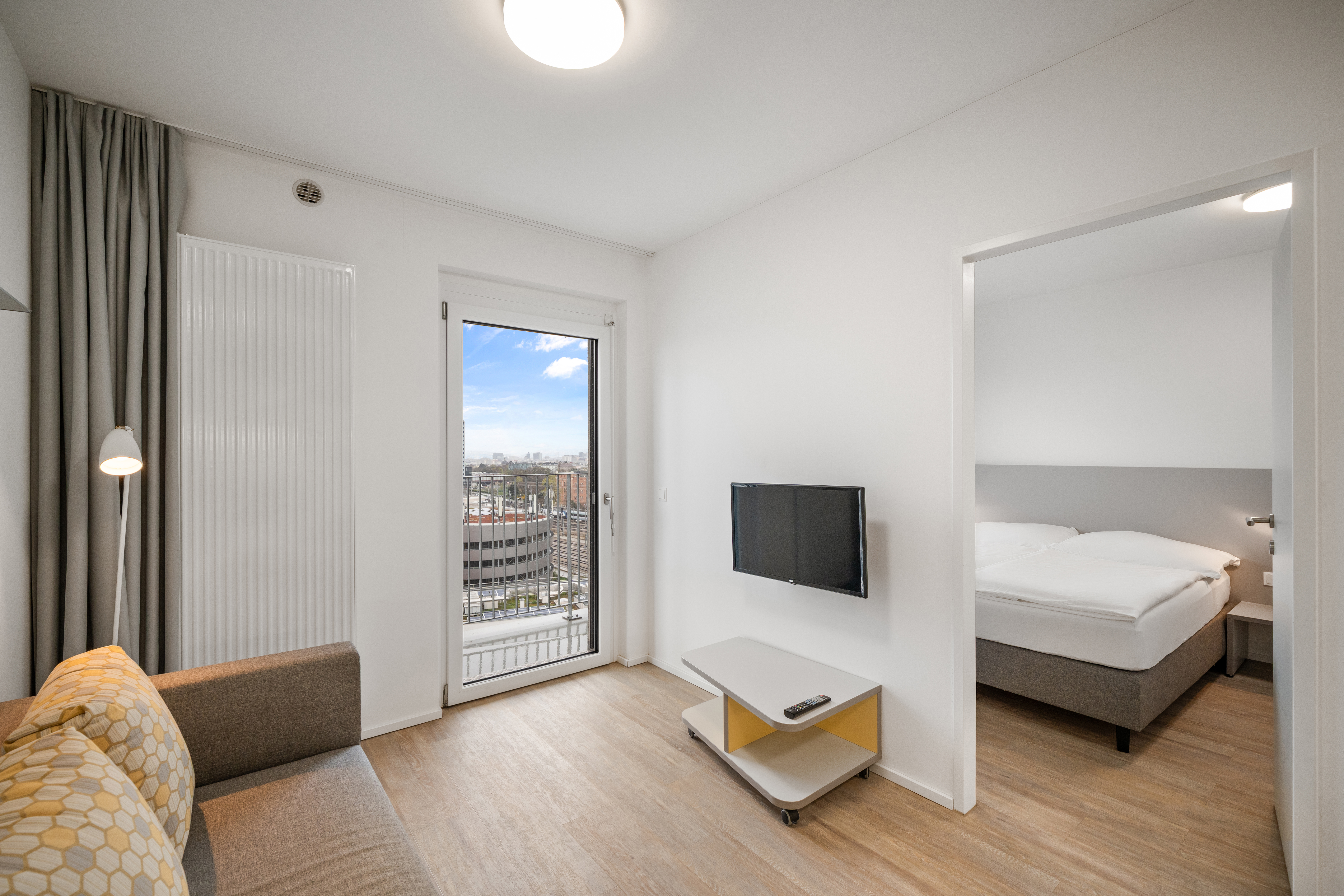 Wohnzimmer mit Sessel, Flachbildschirm und Aussicht über Wien vom Balkon eines möblierten Apartments