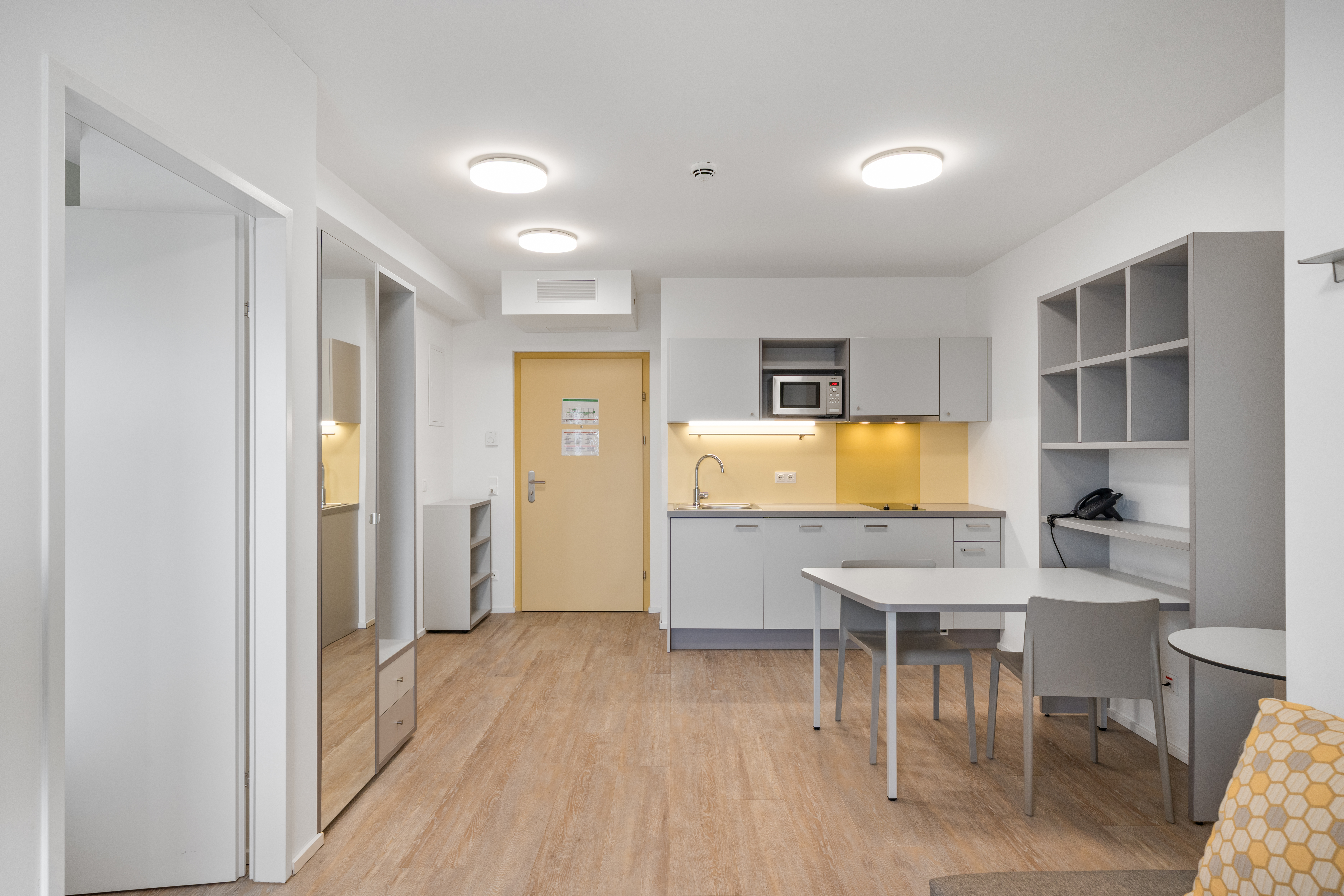 Offene Wohnküche mit Esstisch und Regalen in einem möblierten Apartment Typ M