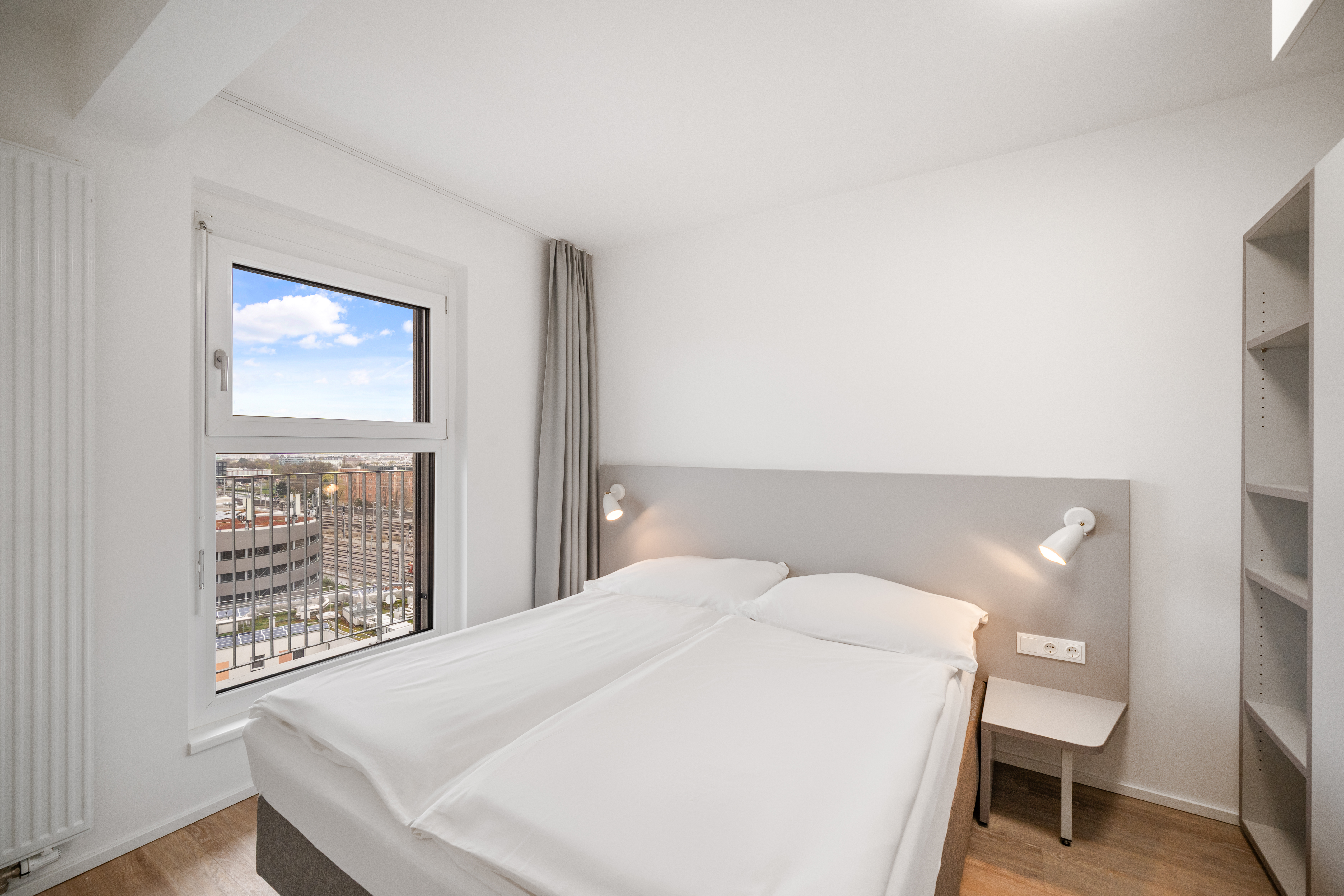Schlafzimmer mit Doppelbett und Fensterblick in einem möblierten Apartment Typ M