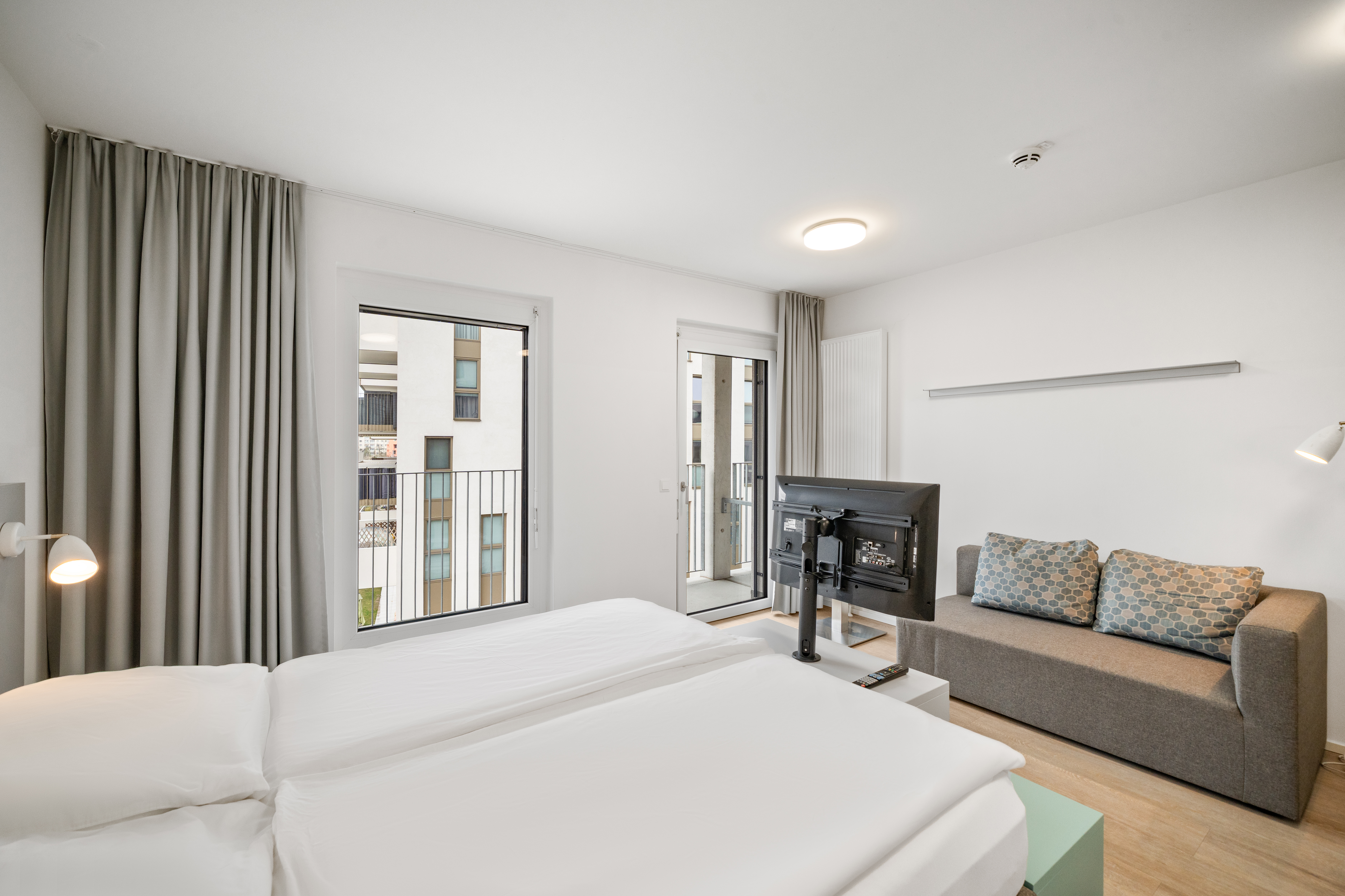 Schlafbereich mit Boxspringbett und Wohnbereich mit Sofa in einem Room4Rent Serviced Apartment der MusicBox Wien