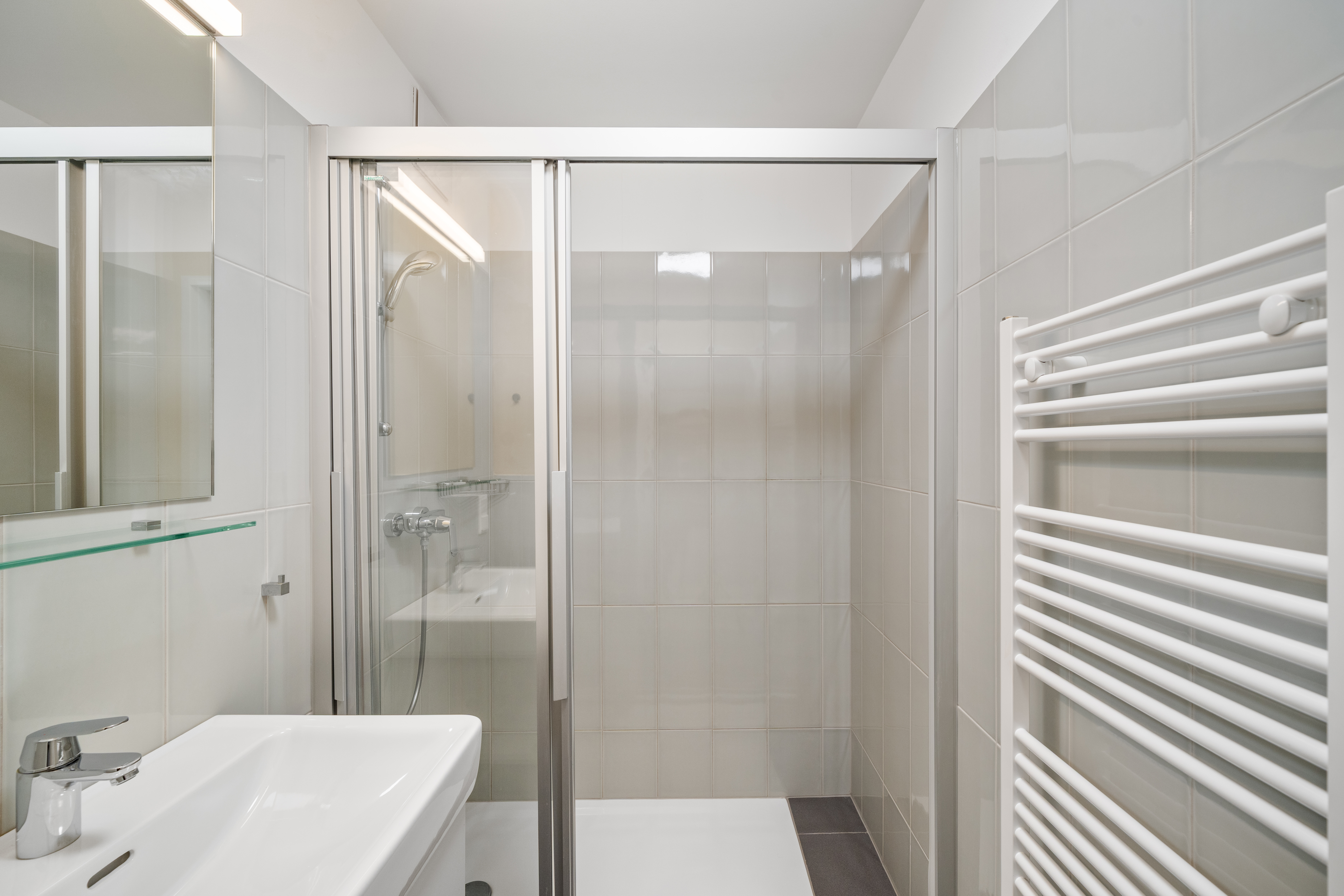 Modernes Badezimmer mit begehbarer Dusche, Waschtisch und Handtuchheizer im möblierten Apartment