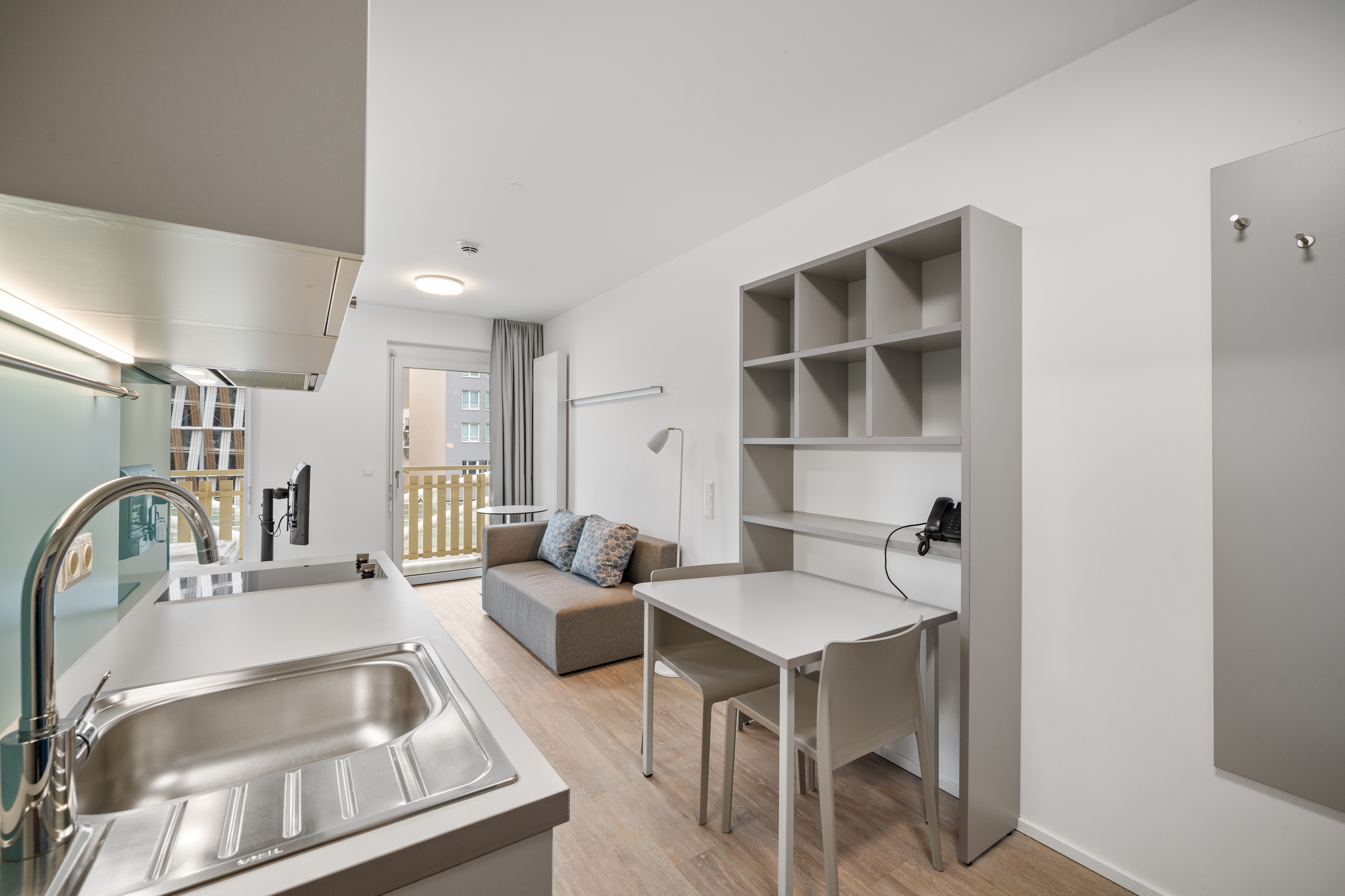 Wohnbereich mit Kitchenette und Arbeitstisch in einem Room4Rent XS Balcony Serviced Apartment
