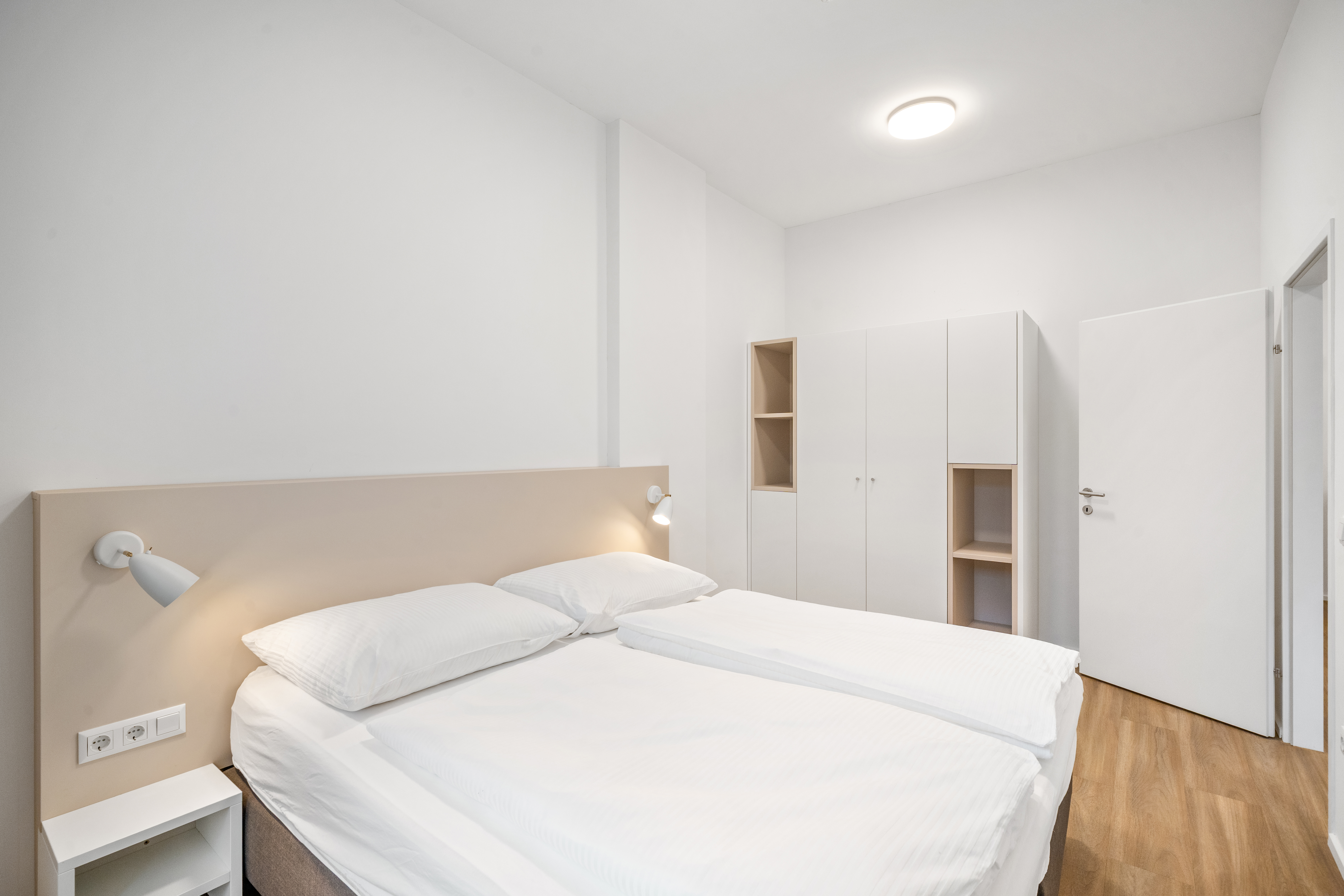 Schlafzimmer mit Doppelbett und moderner weißer Schrankwand im Room4Rent Serviced Apartment Typ L