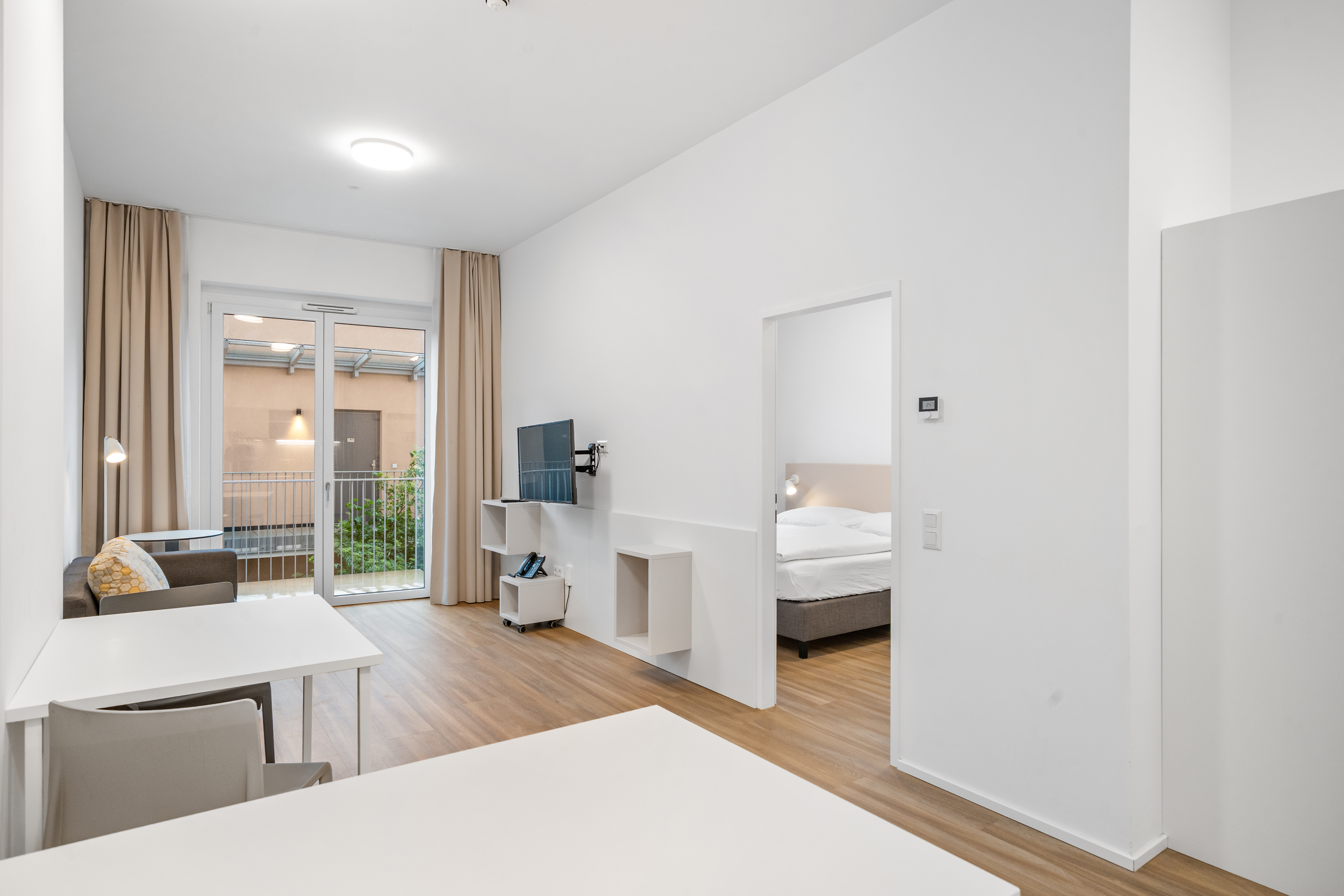 Wohnbereich mit Arbeitsplatz, Fernseher und Balkonzugang in einem möblierten Apartment im Q-Tower