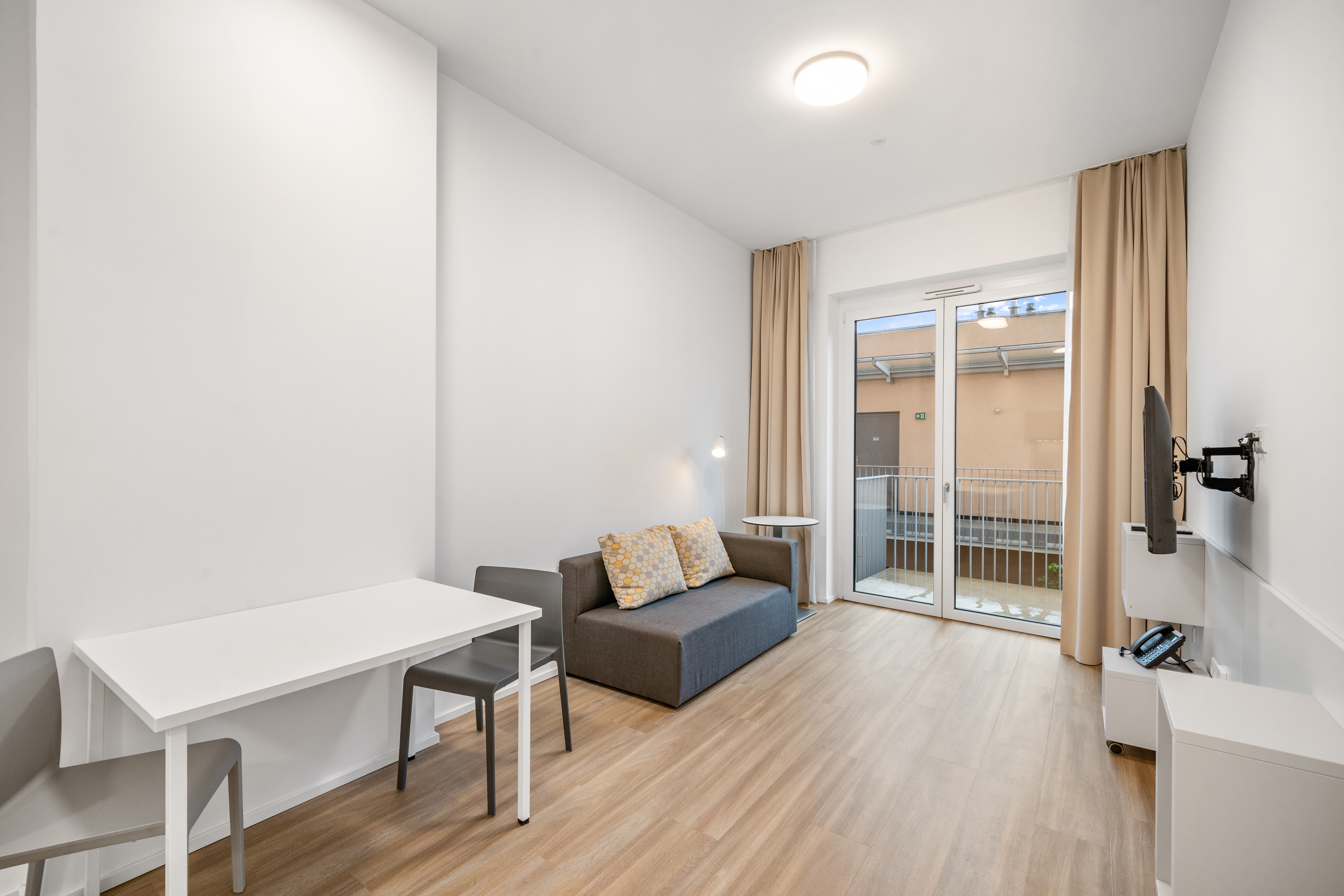 Wohnbereich mit Sofa, Arbeitsplatz und Balkonzugang in einem Room4Rent möblierten Apartment Typ L im Q-Tower