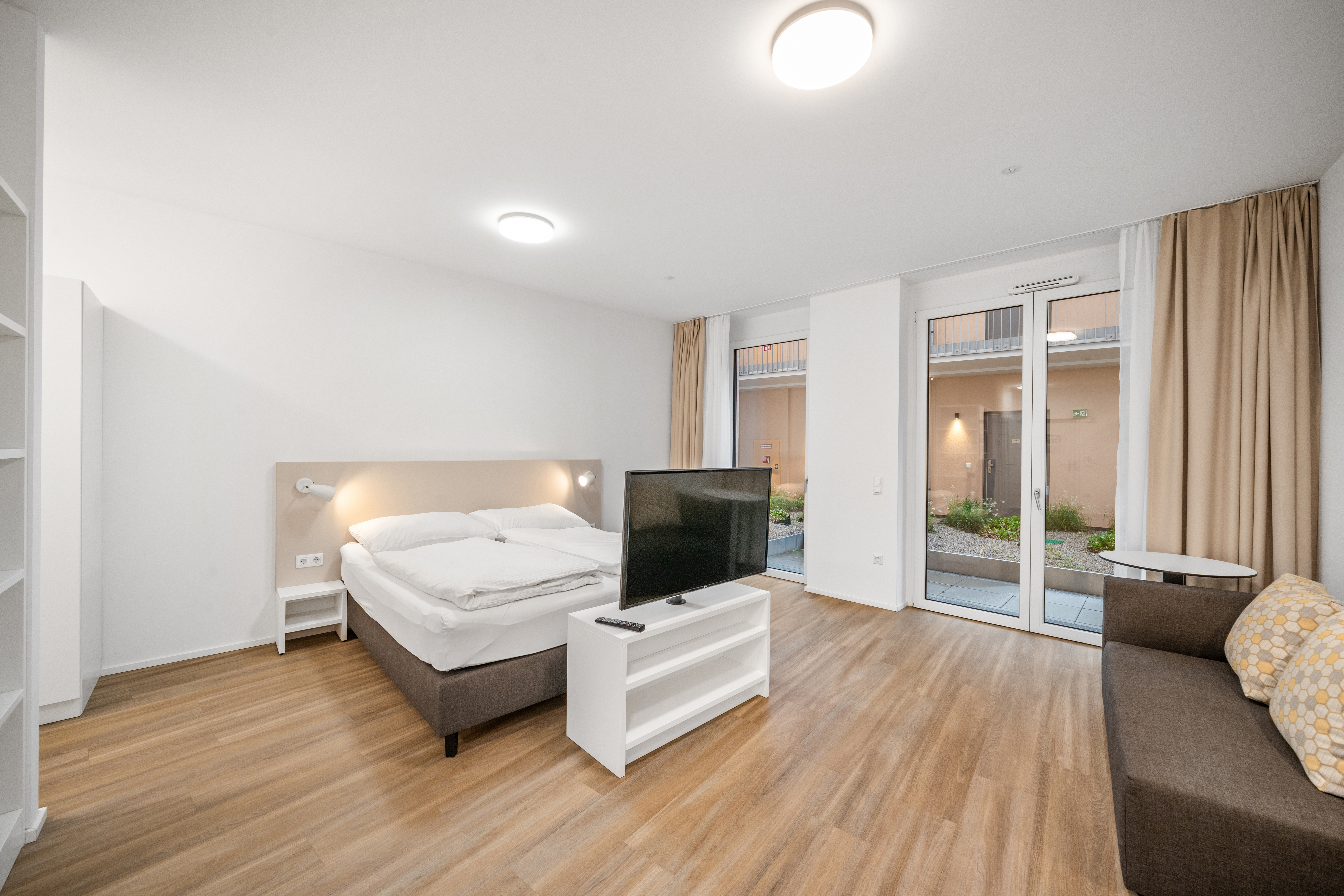 Schlaf- und Wohnbereich mit Bett, Fernseher und Zugang zum Balkon in einem möblierten Apartment im Q-Tower