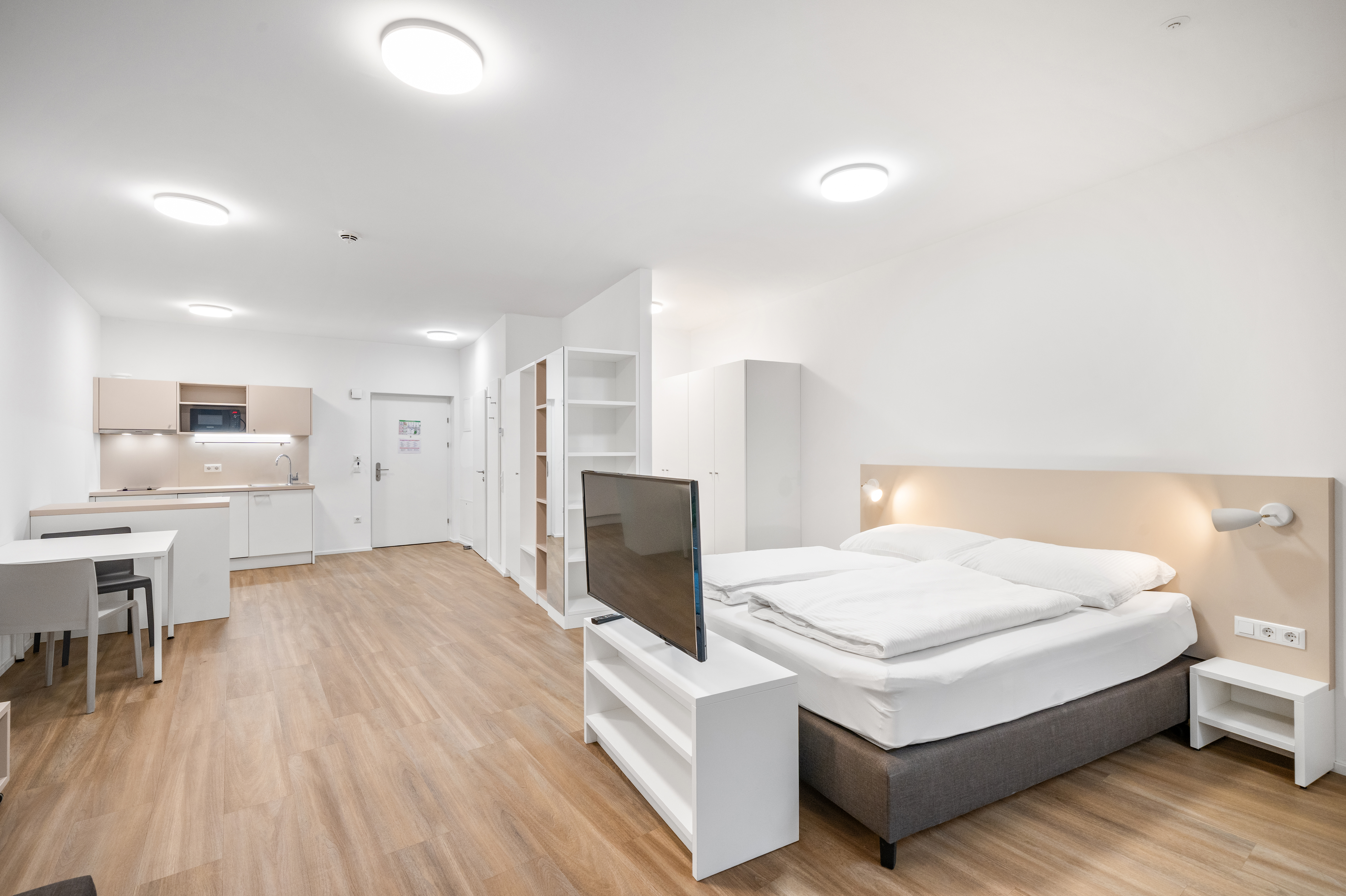 Schlaf- und Wohnbereich mit Doppelbett, Fernseher und offener Küche in einem möblierten Serviced Apartment Typ L im Q-Tower