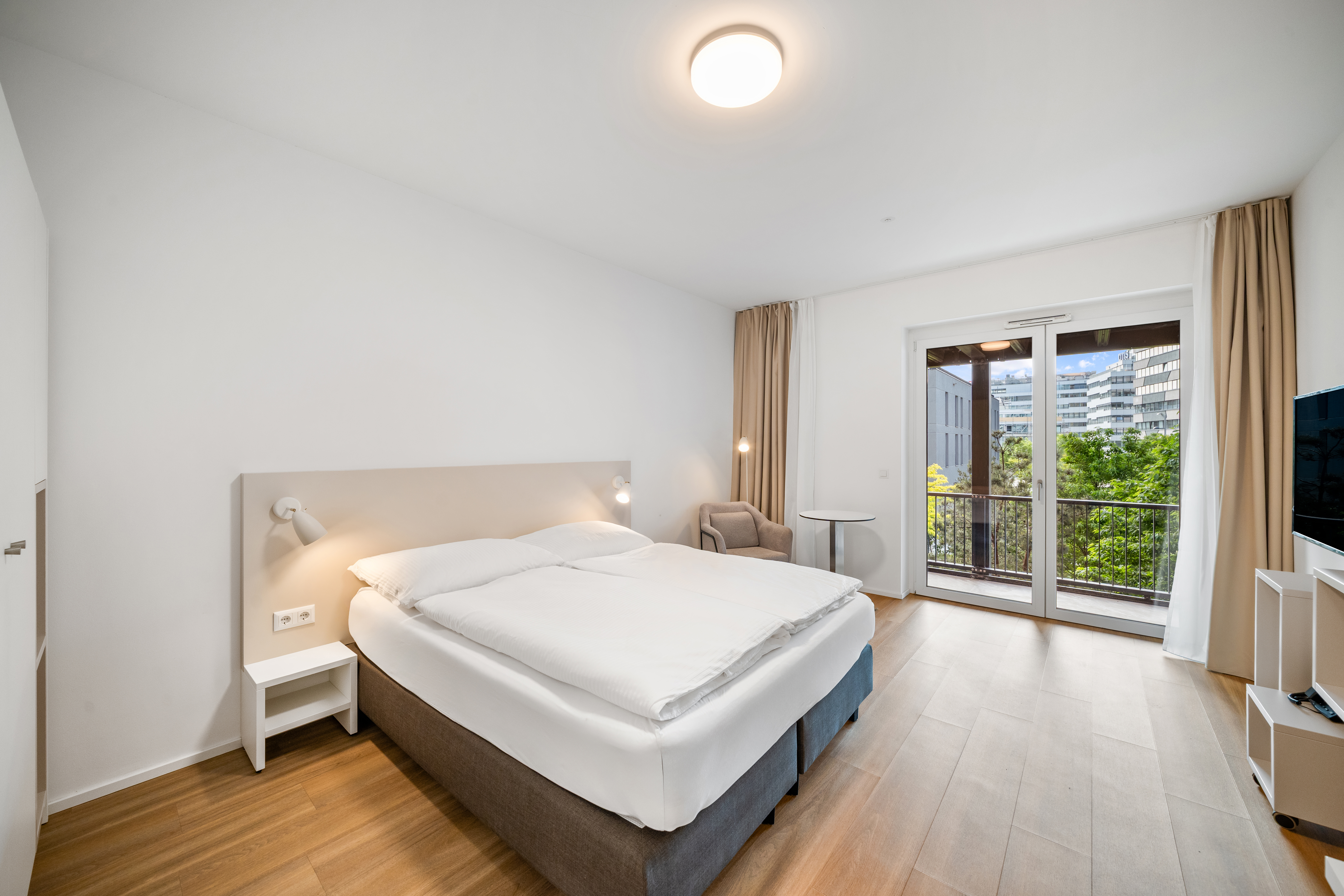 Schlafzimmer mit Doppelbett, Balkon und Stadtblick in einem möblierten Apartment im Q-Tower Wien