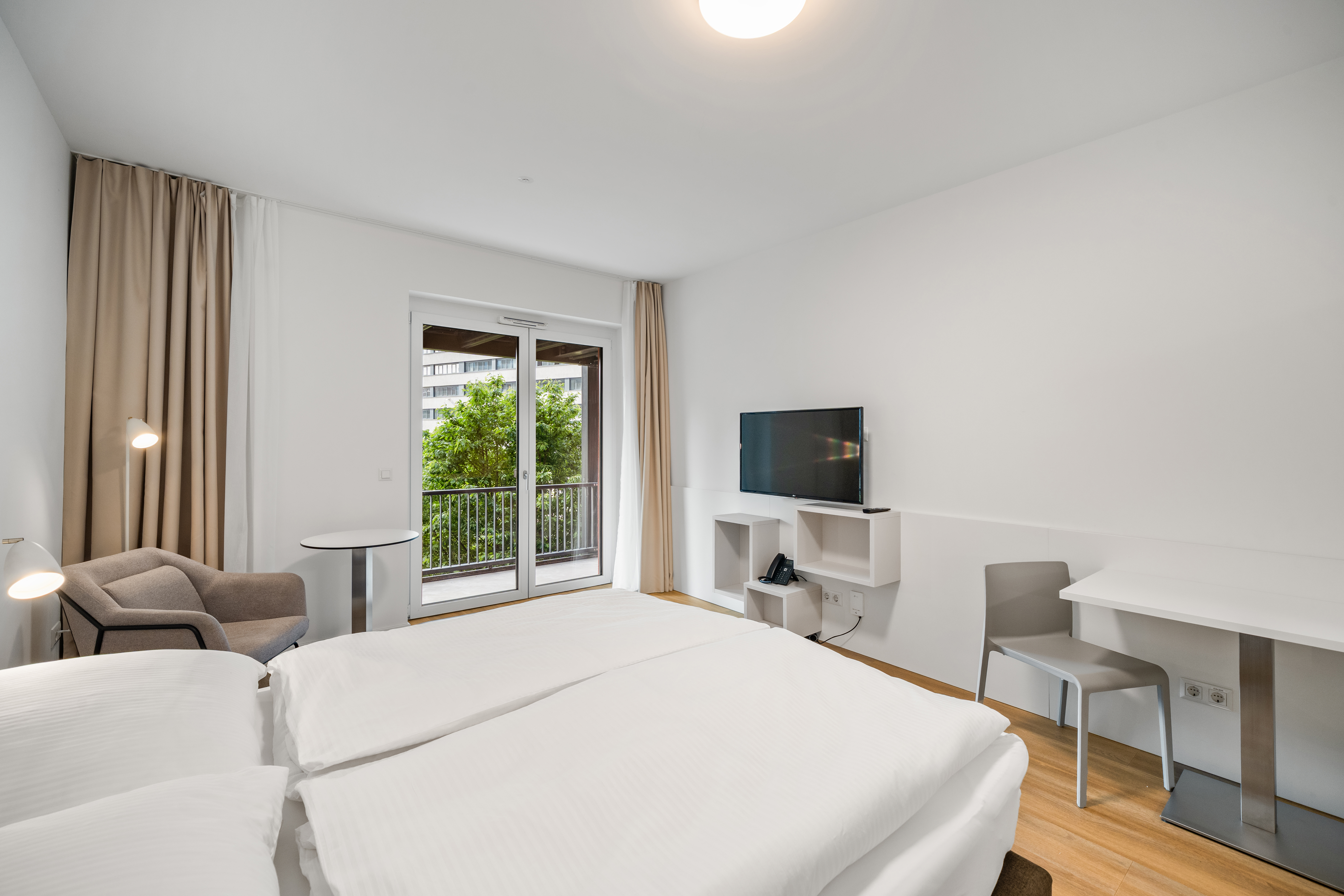Schlafzimmer mit zwei Betten, Balkon und Arbeitsplatz in einem Room4Rent Serviced Apartment im Q-Tower Wien
