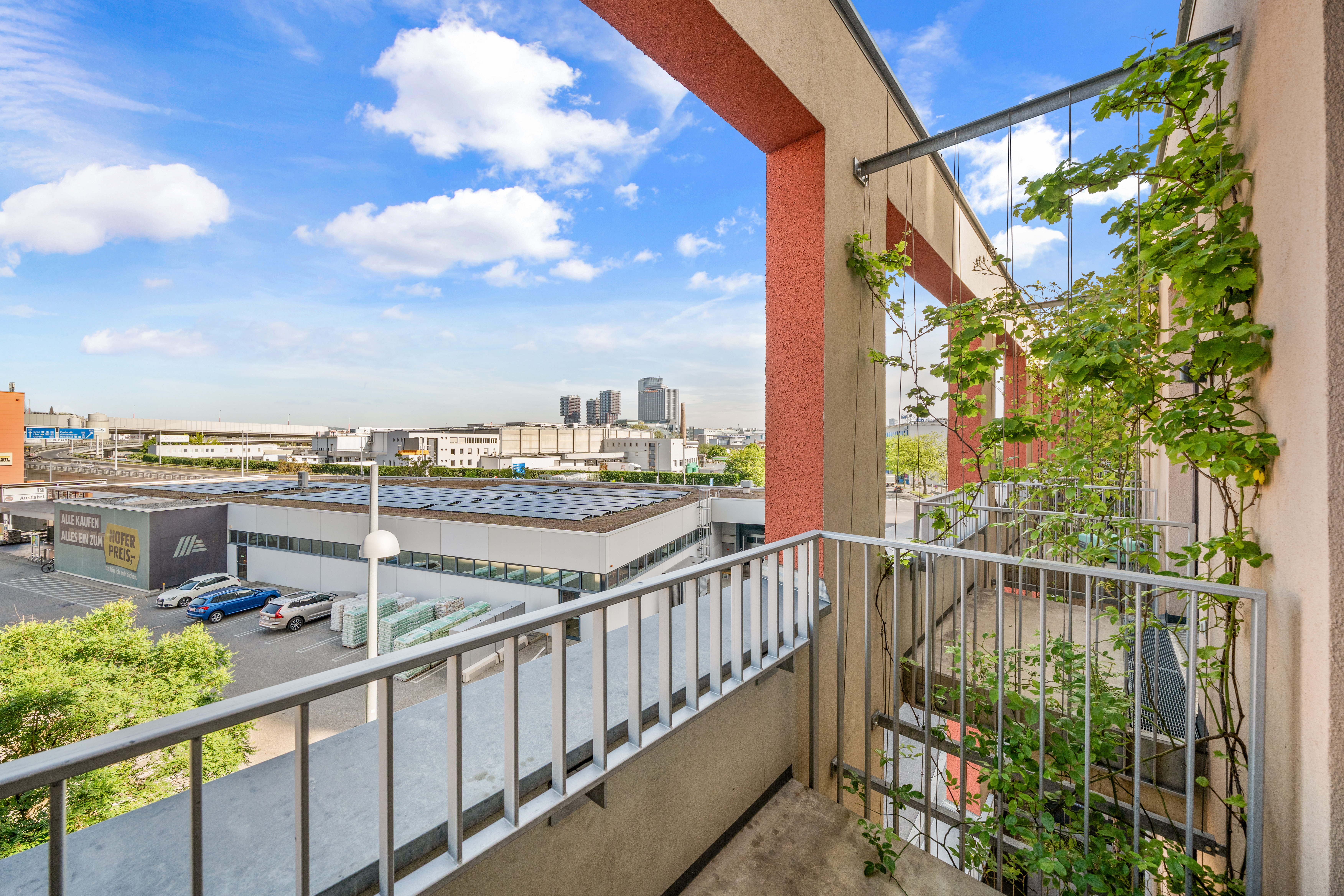 Balkon mit Metallgeländer und Ausblick auf die Wiener Skyline, umgeben von grüner Vegetation