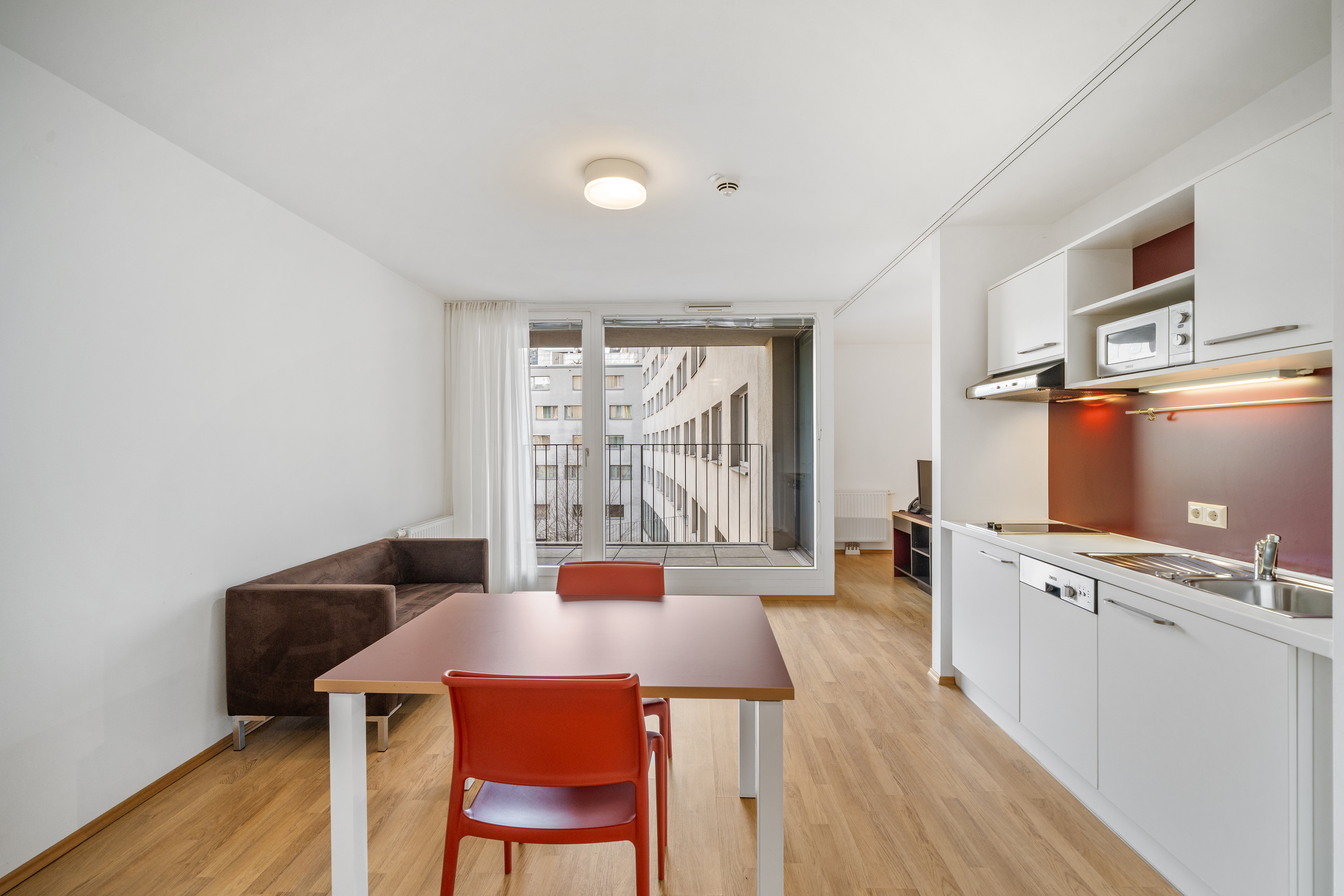 Wohnbereich mit Essbereich, offener Küche und Balkonzugang in einem möblierten Room4Rent Serviced Apartment Typ M