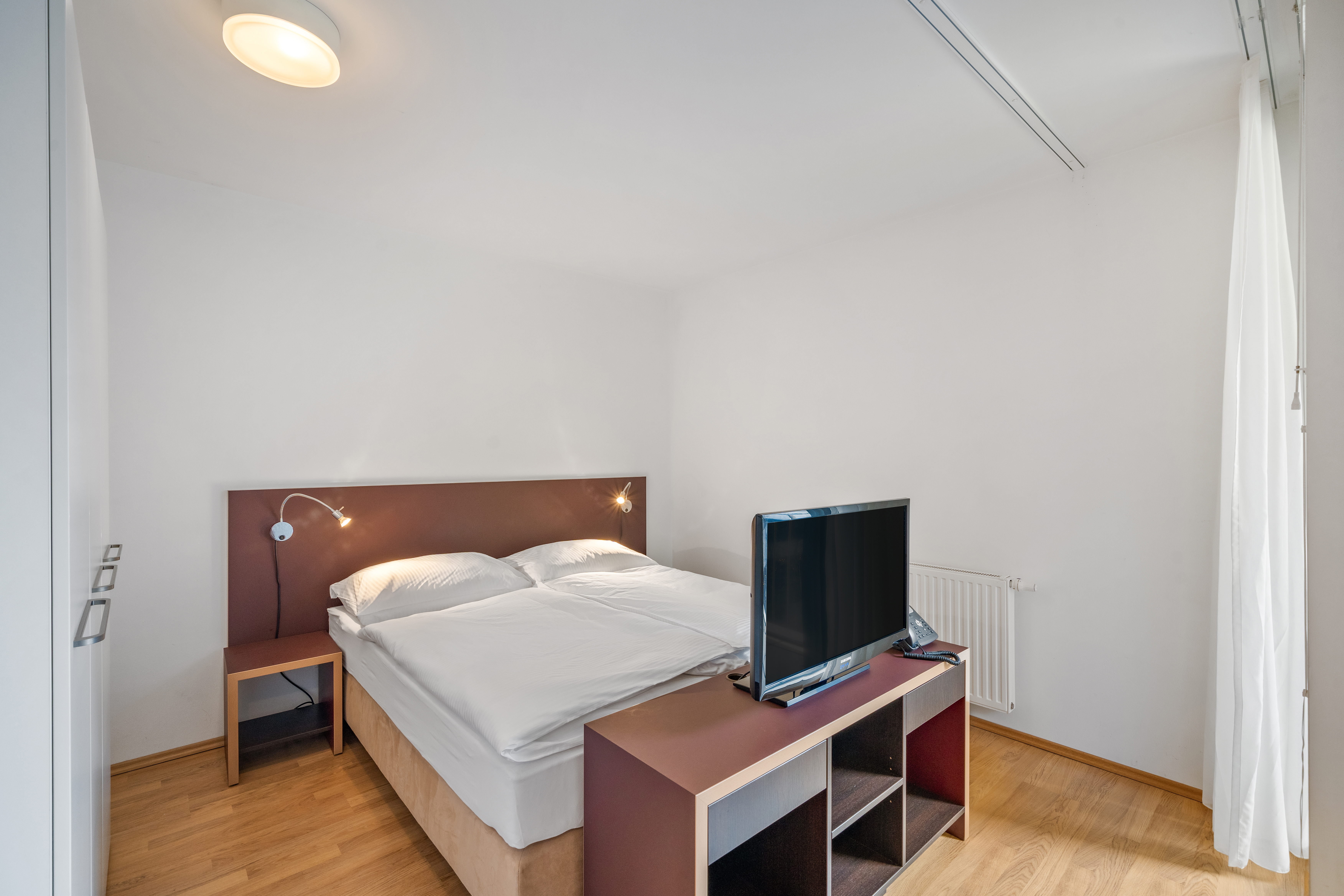 Schlafzimmer mit Doppelbett, braunem Kopfteil mit Leseleuchten und TV-Gerät auf Regal in Room4Rent S Balcony Apartment am Storchen&shy;grund