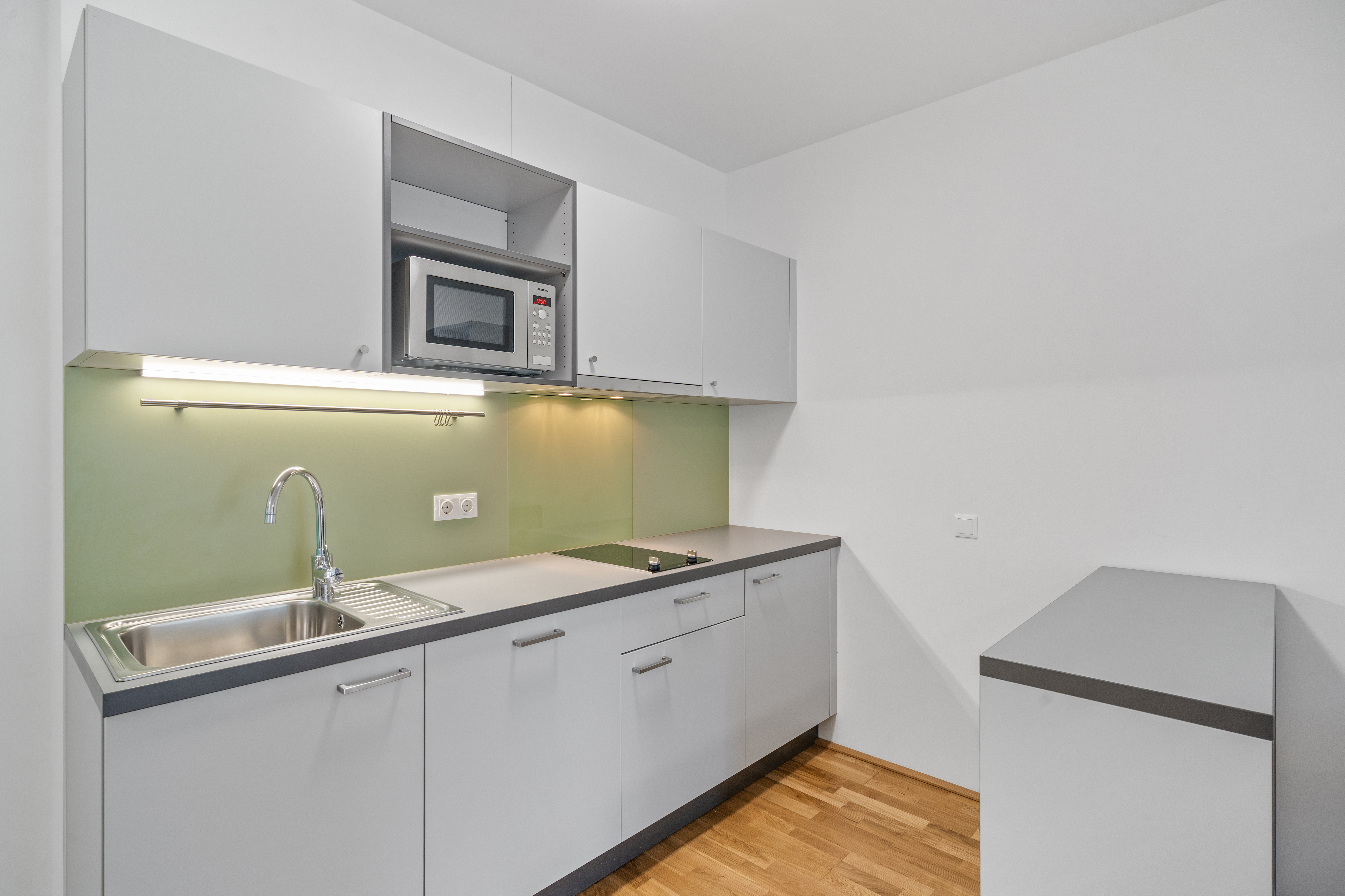 Moderne Küchenzeile mit grüner Rückwand, Spüle und Mikrowellengerät in einem Room4Rent Apartment