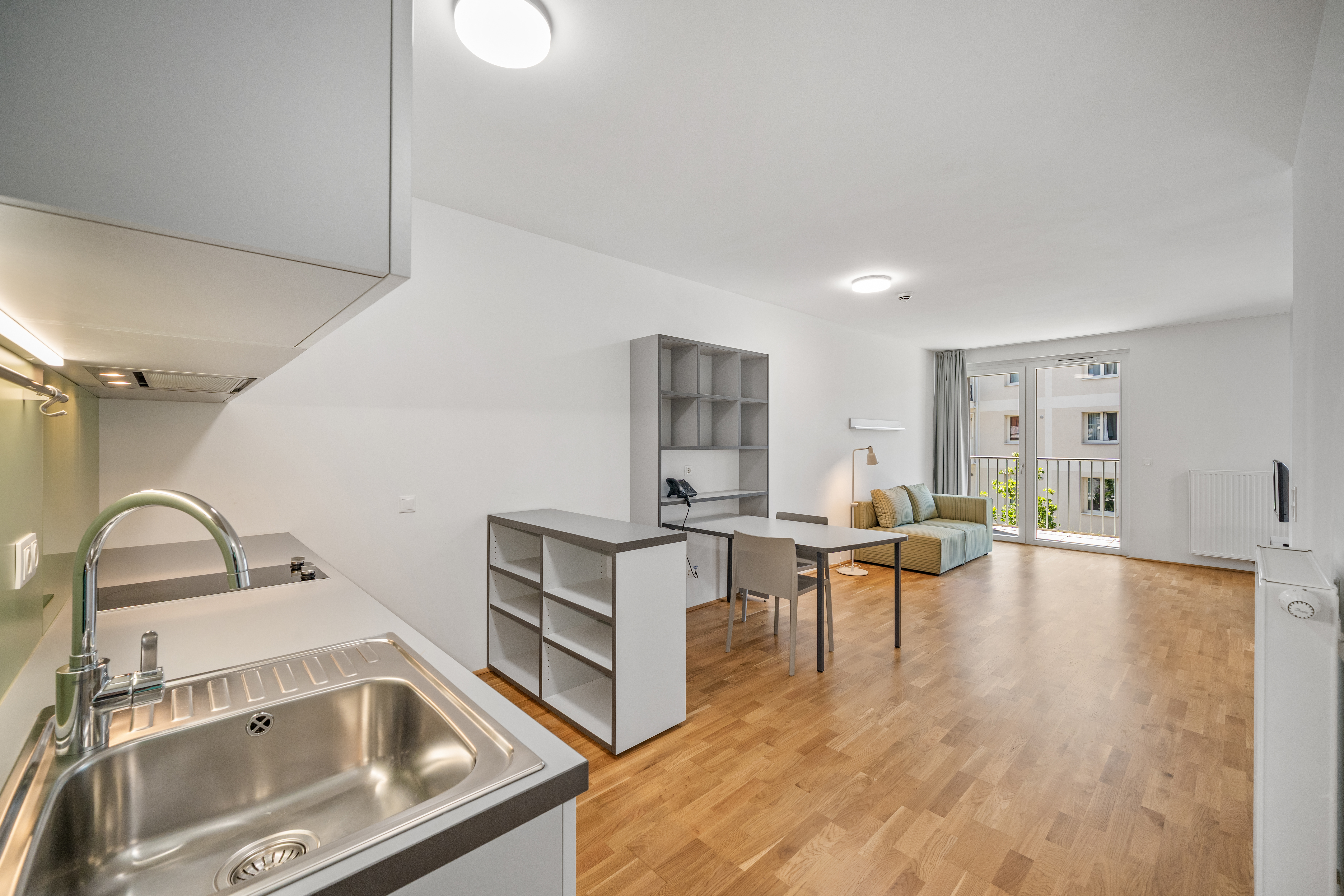 Wohnbereich eines Room4Rent Apartments mit offener Küchenzeile, Esstisch und Balkonzugang