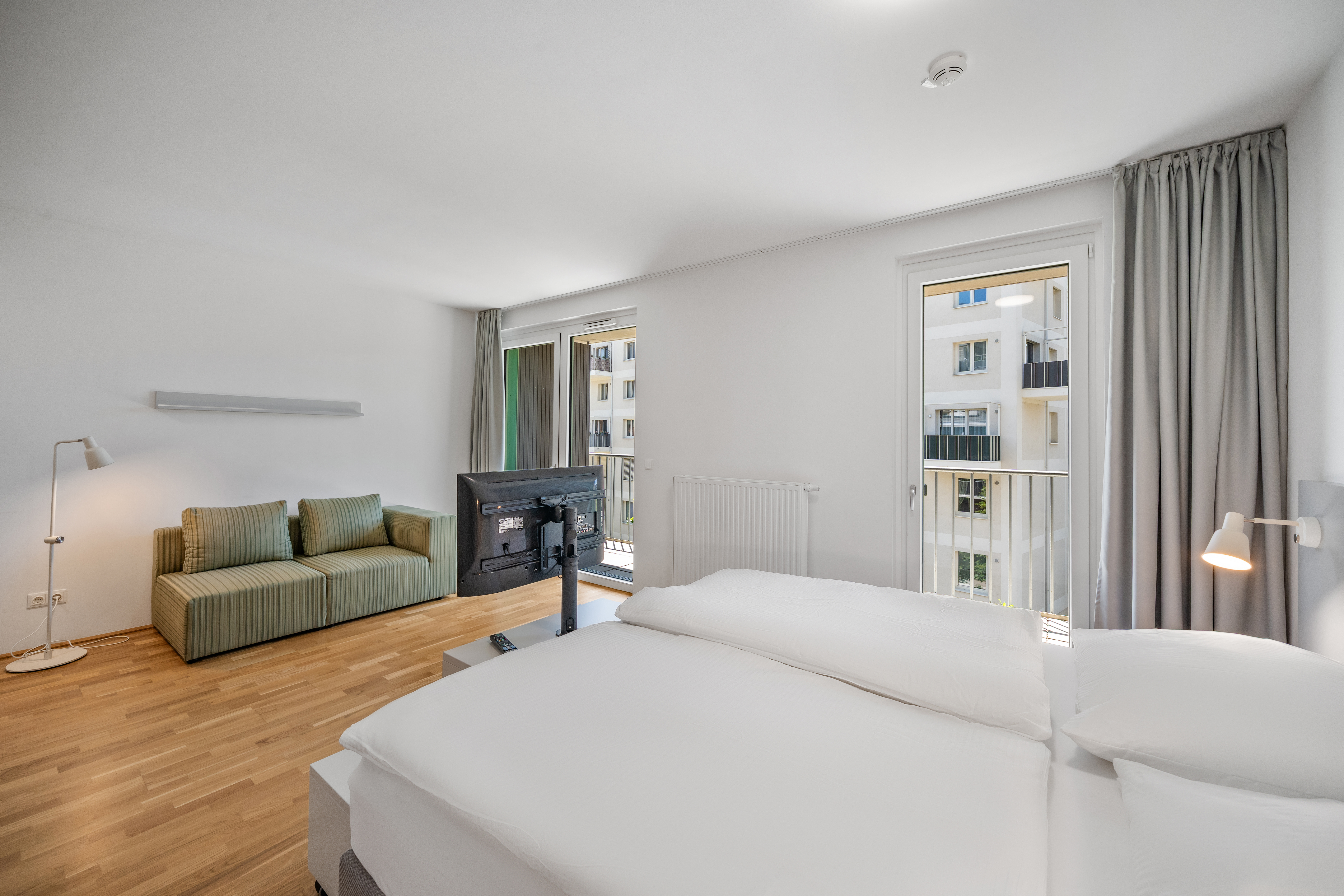 Wohnbereich mit Schlafzone, Sofa und Küchenzeile in einem Room4Rent Apartment Typ L Balcony