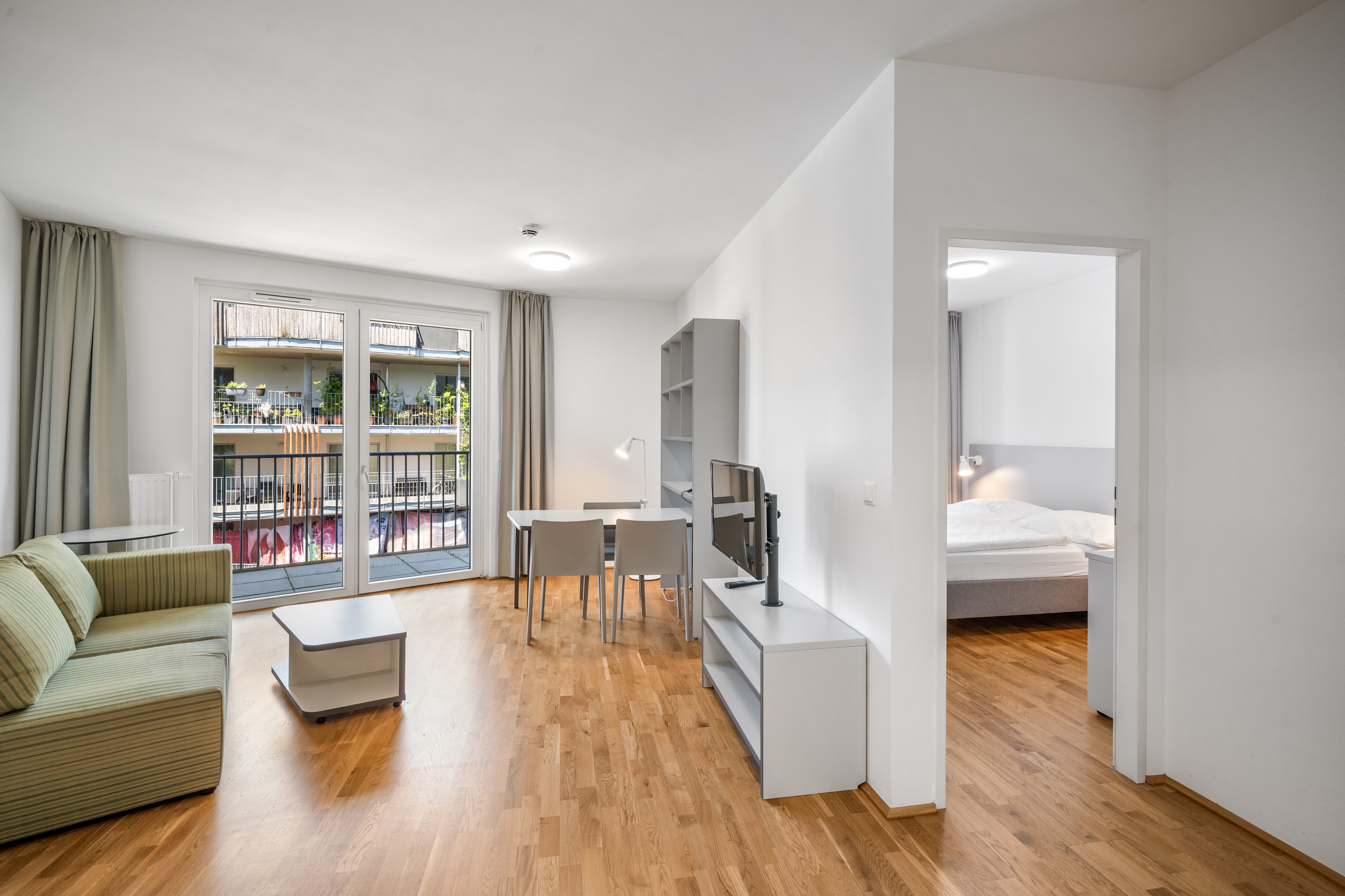 Wohnbereich mit Sofa, Esstisch und Zugang zum Balkon im möblierten Apartment Typ M mit Balkon in Vienna Academic Guesthouse