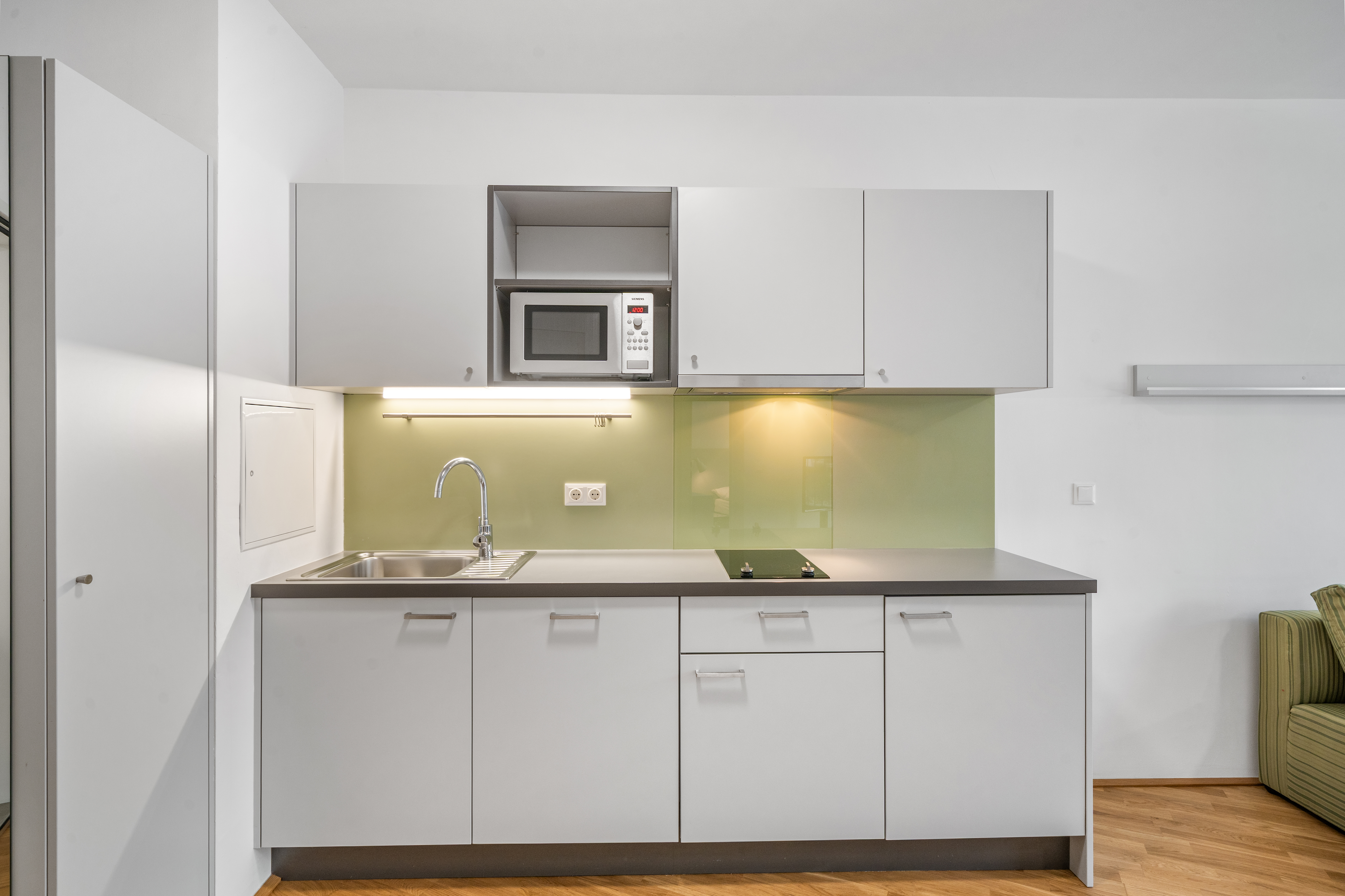 Küche mit weißen Schrankelementen, grüner Rückwand und Edelstahlarmaturen in einem Room4Rent Serviced Apartment