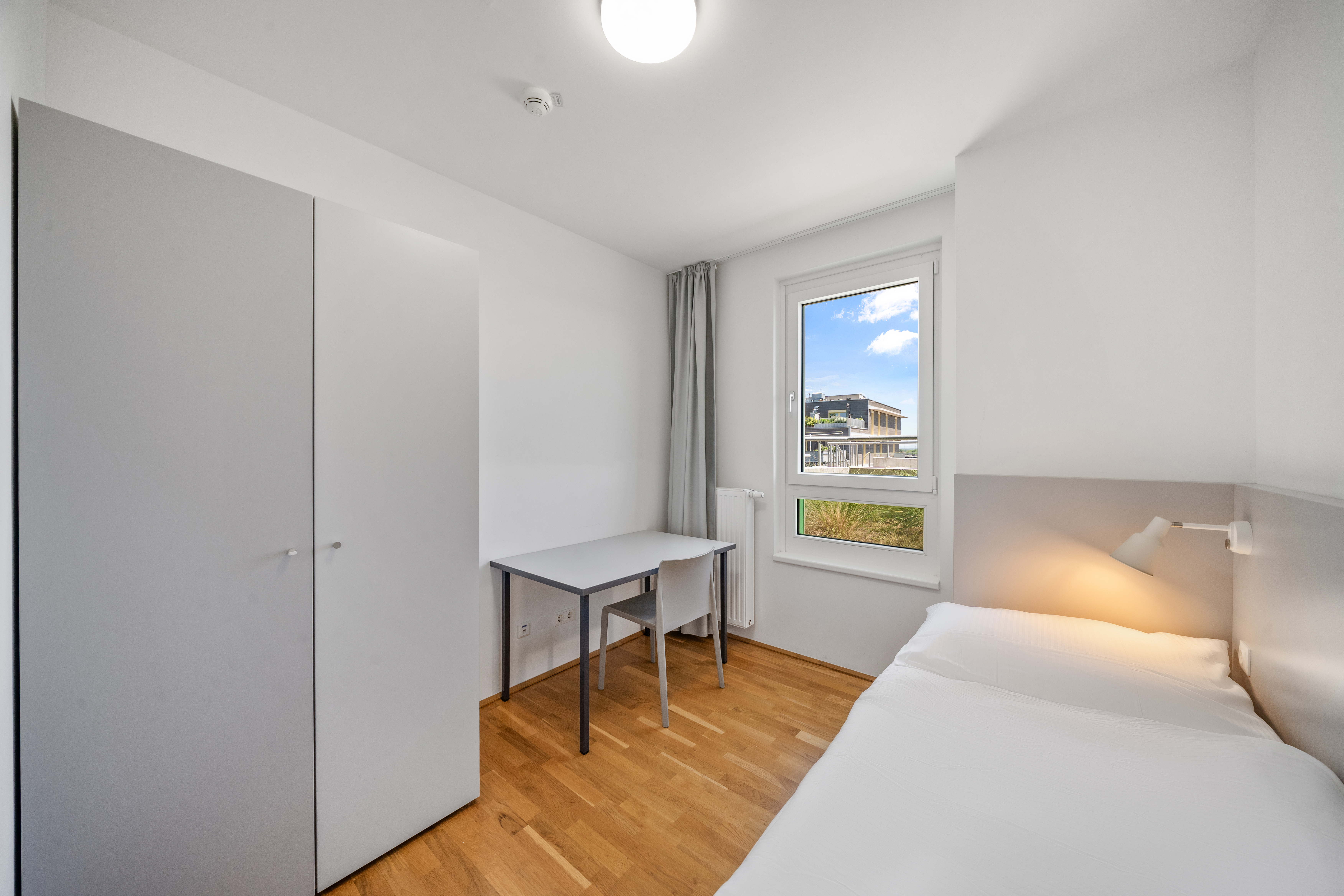 Schlafbereich eines leeren XL-Apartments mit Doppelbett, Schreibtisch und großem Fenster