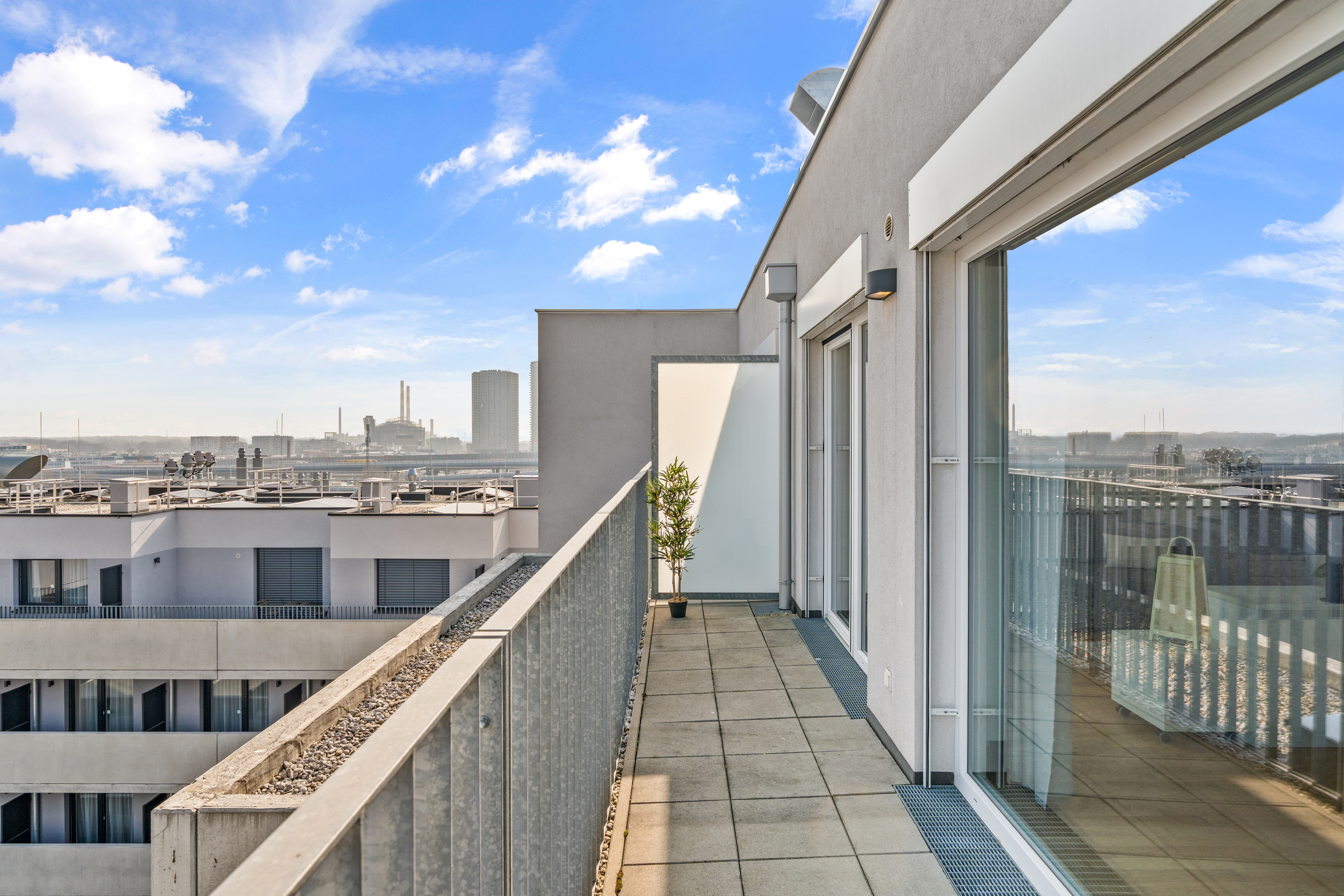 Moderner Balkon mit Glasschiebetüren, Metallgeländer und Blick auf die Industrielandschaft
