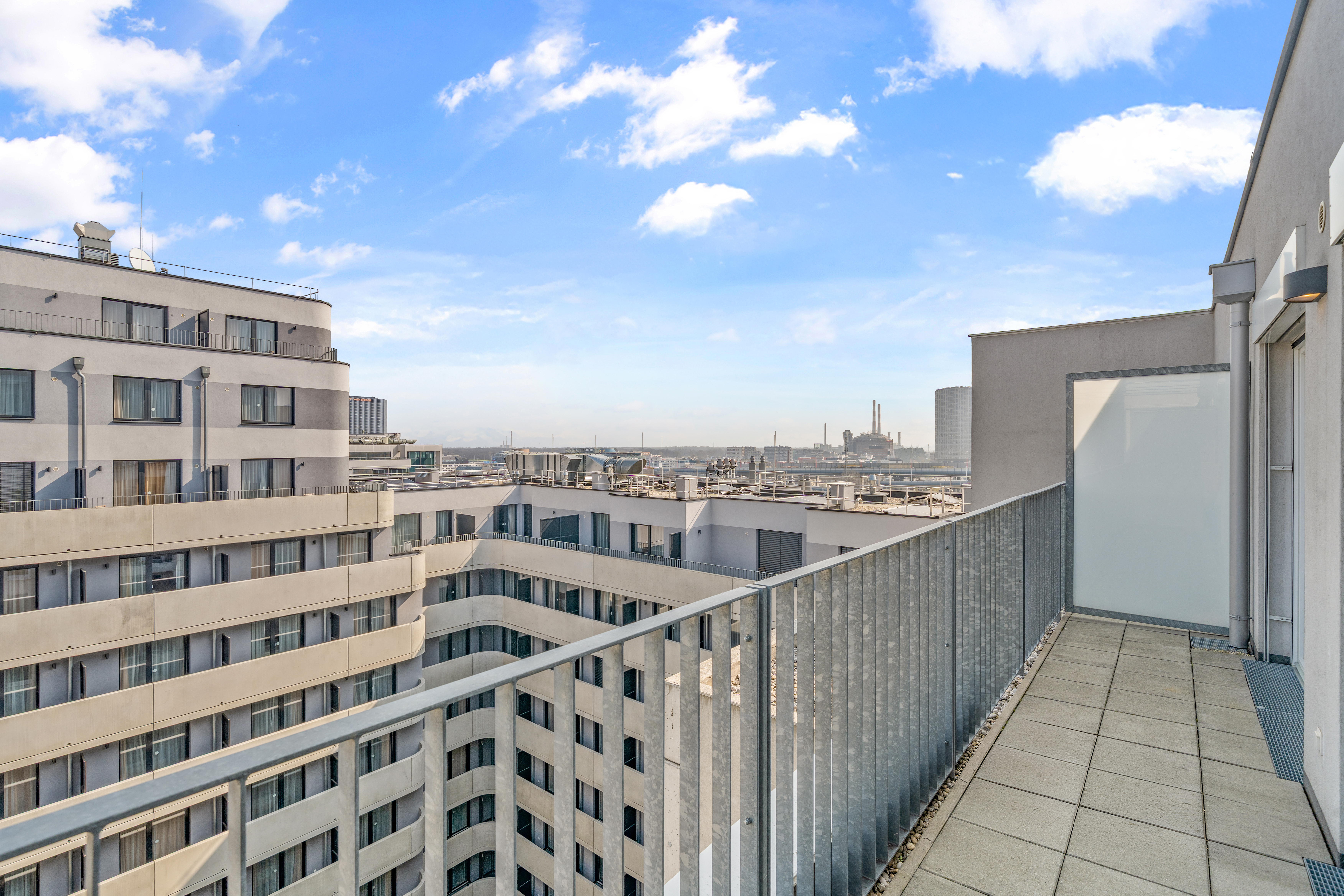 Stadtblick von einem Balkon mit Blick auf mehrstöckige Wohngebäude und industrielle Skyline unter blauem Himmel