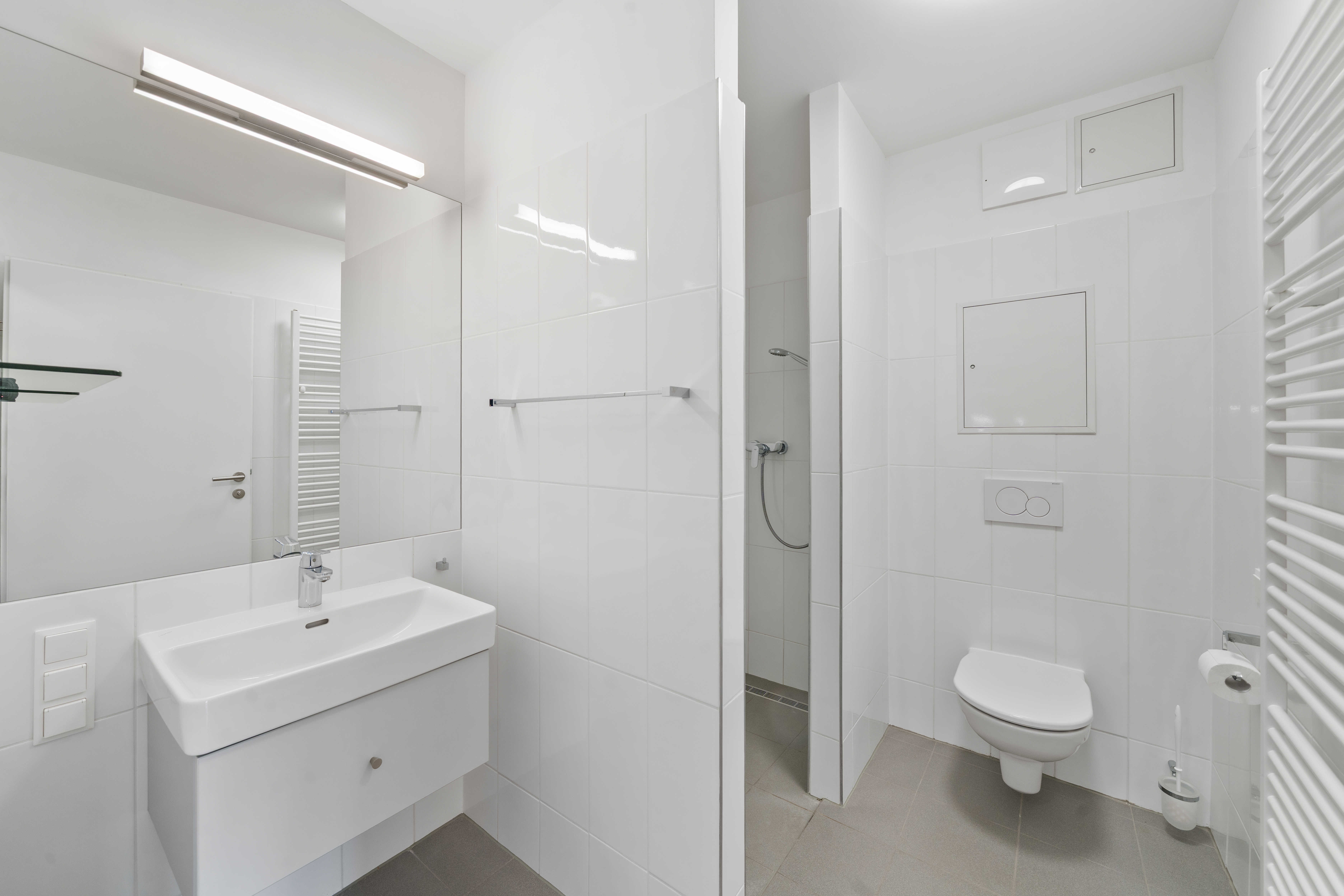 Helles Badezimmer mit weißen Fliesen, Waschbecken, Spiegel, Dusche und Handtuchständer