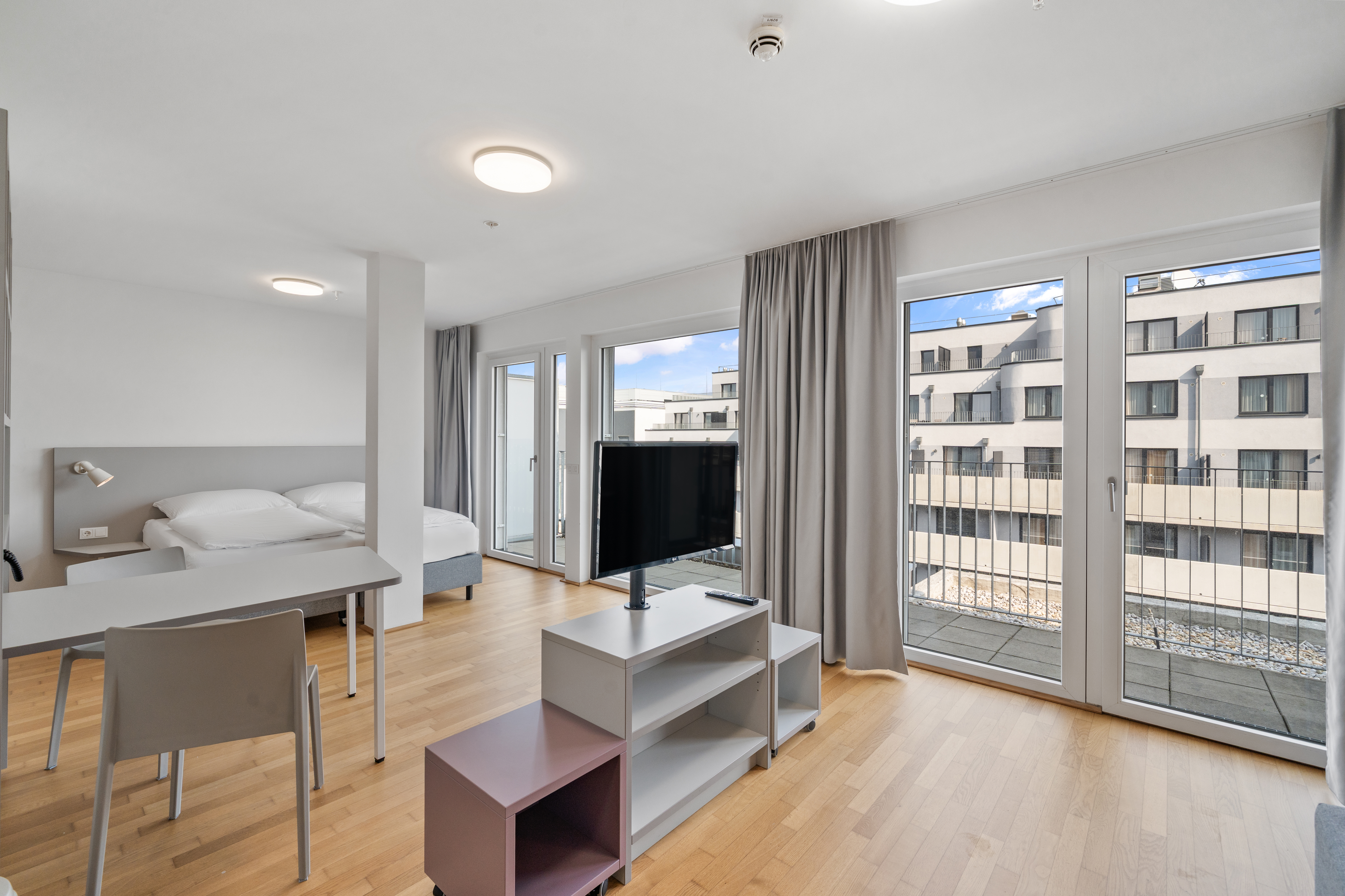 Modernes Wohnzimmer mit Schlafbereich, Sofa, Fernseher und Balkontüren mit Ausblick