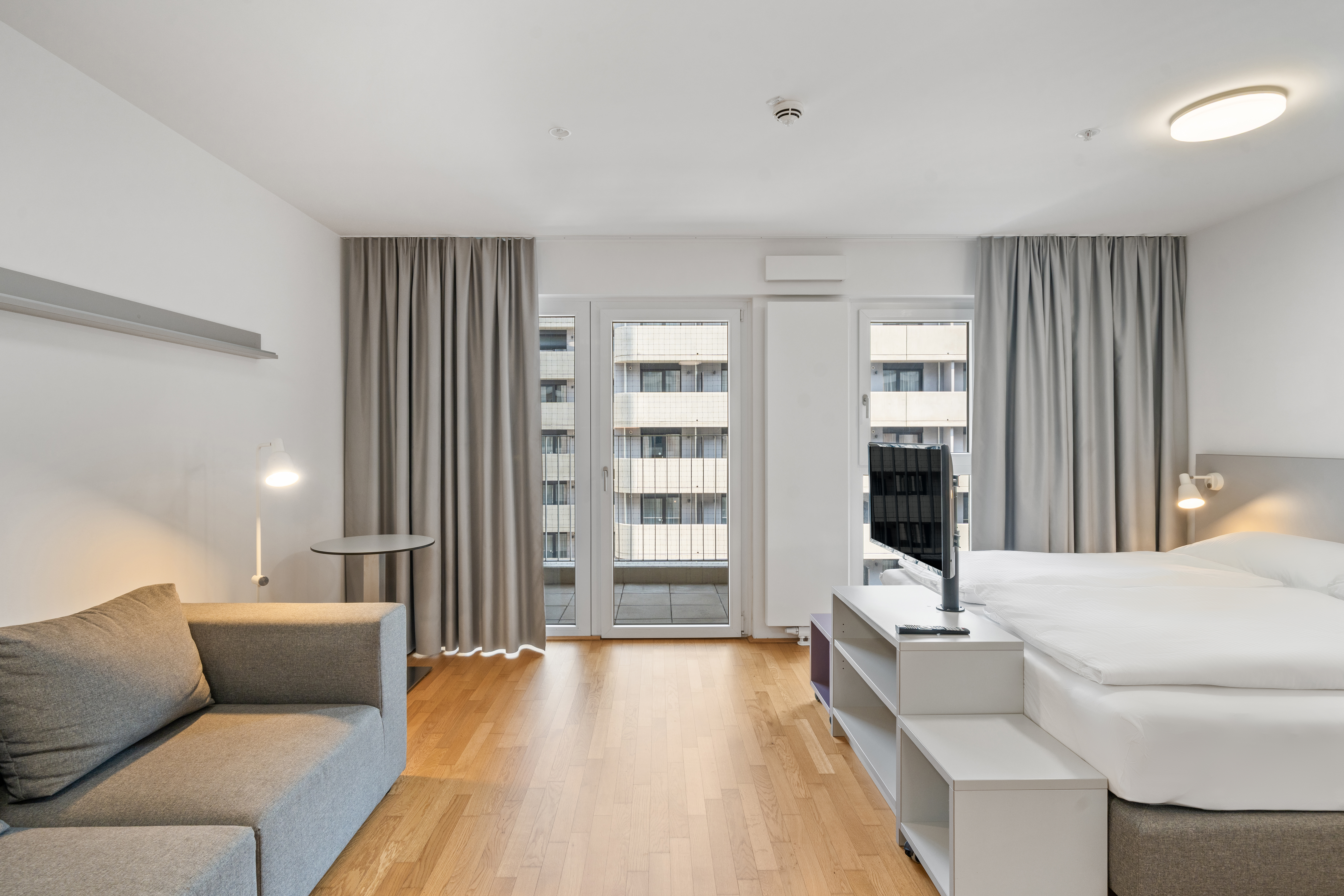 Schlafbereich in einem Room4Rent Serviced Apartment mit Bett, Sofa und Fenster mit Ausblick