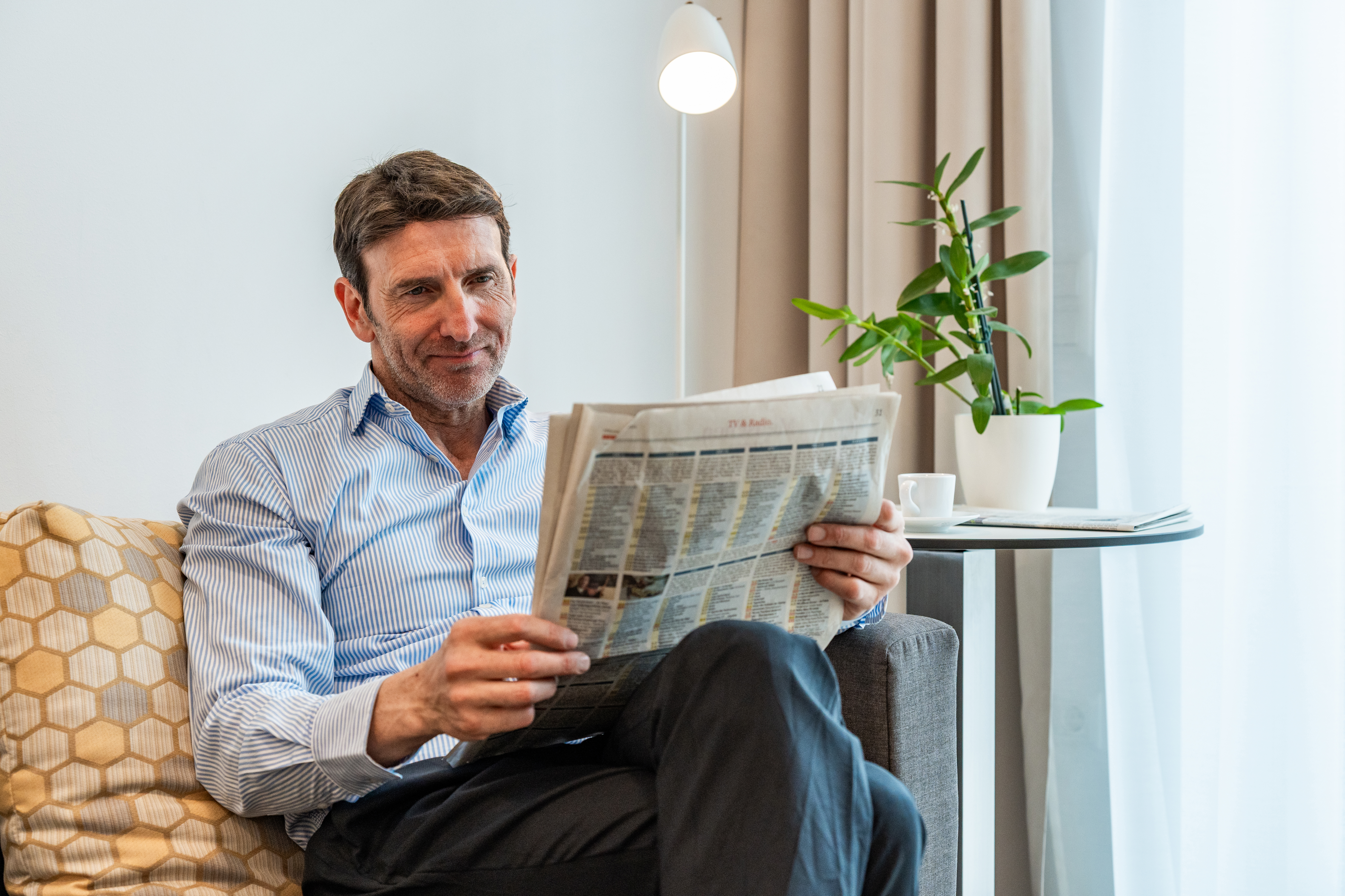 Ein R4R Business Kunde liest entspannt eine Zeitung in seinem Apartment, neben ihm steht ein kleiner Tisch mit einem Kaffee.