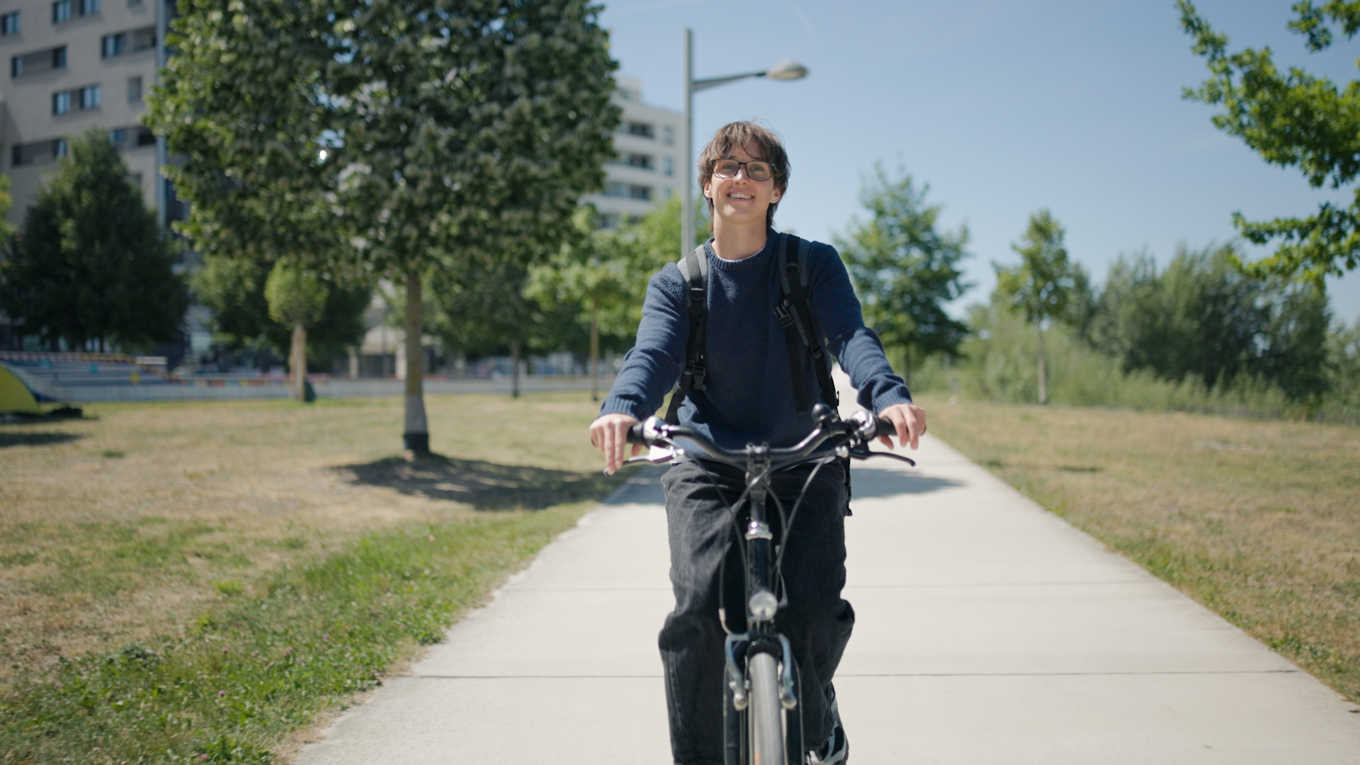 Mann auf Fahrrad auf sonnigem Betonweg mit Bäumen und Wohngebäude im Hintergrund
