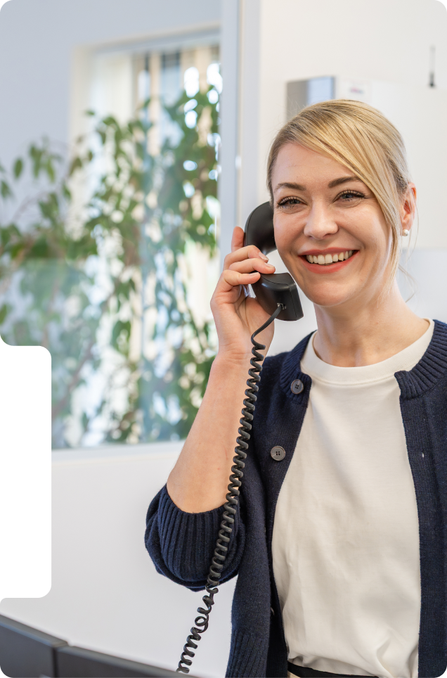 Frau telefoniert mit schwarzem Telefon, trägt marineblaue Strickjacke und weißes Shirt