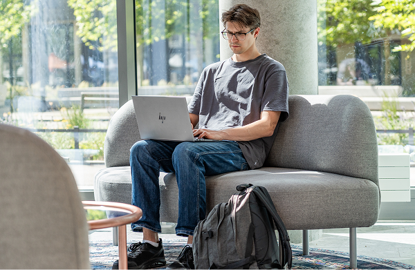 Junger Mann mit Laptop auf grauem Sofa in modernem, hellen Apartment